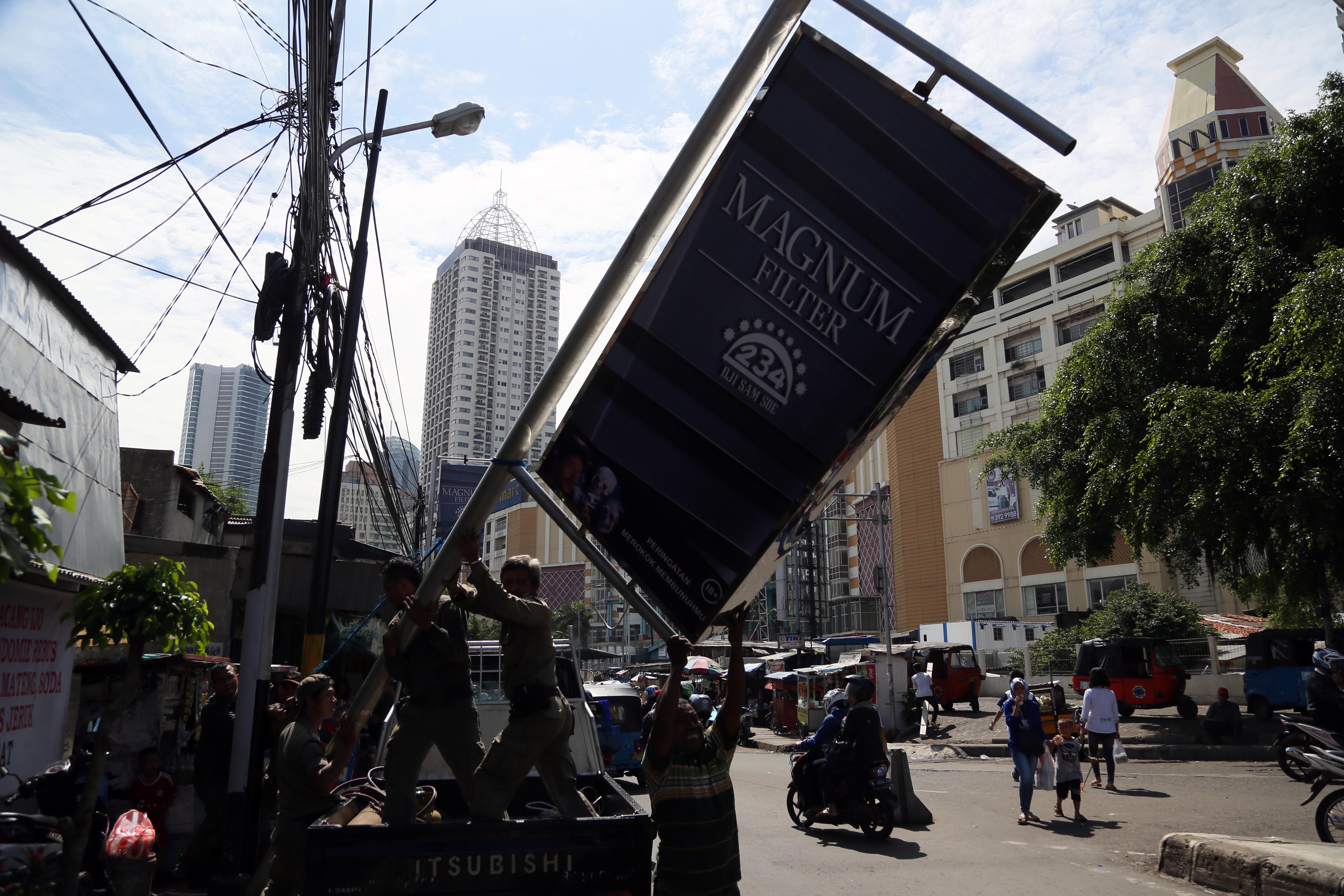 Potret petugas saat menurunkan papan reklame produk rokok.