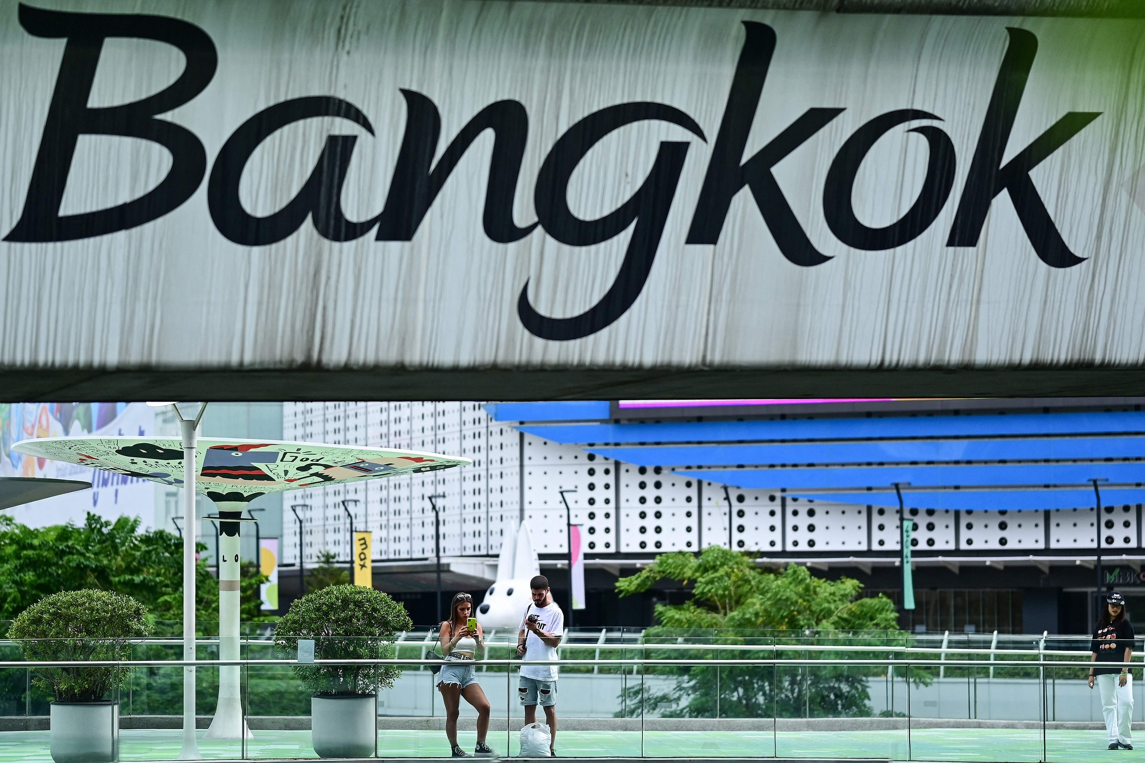 Potret turis berdiri di bawah jembatan dengan tulisan 'Bangkok', Thailand.