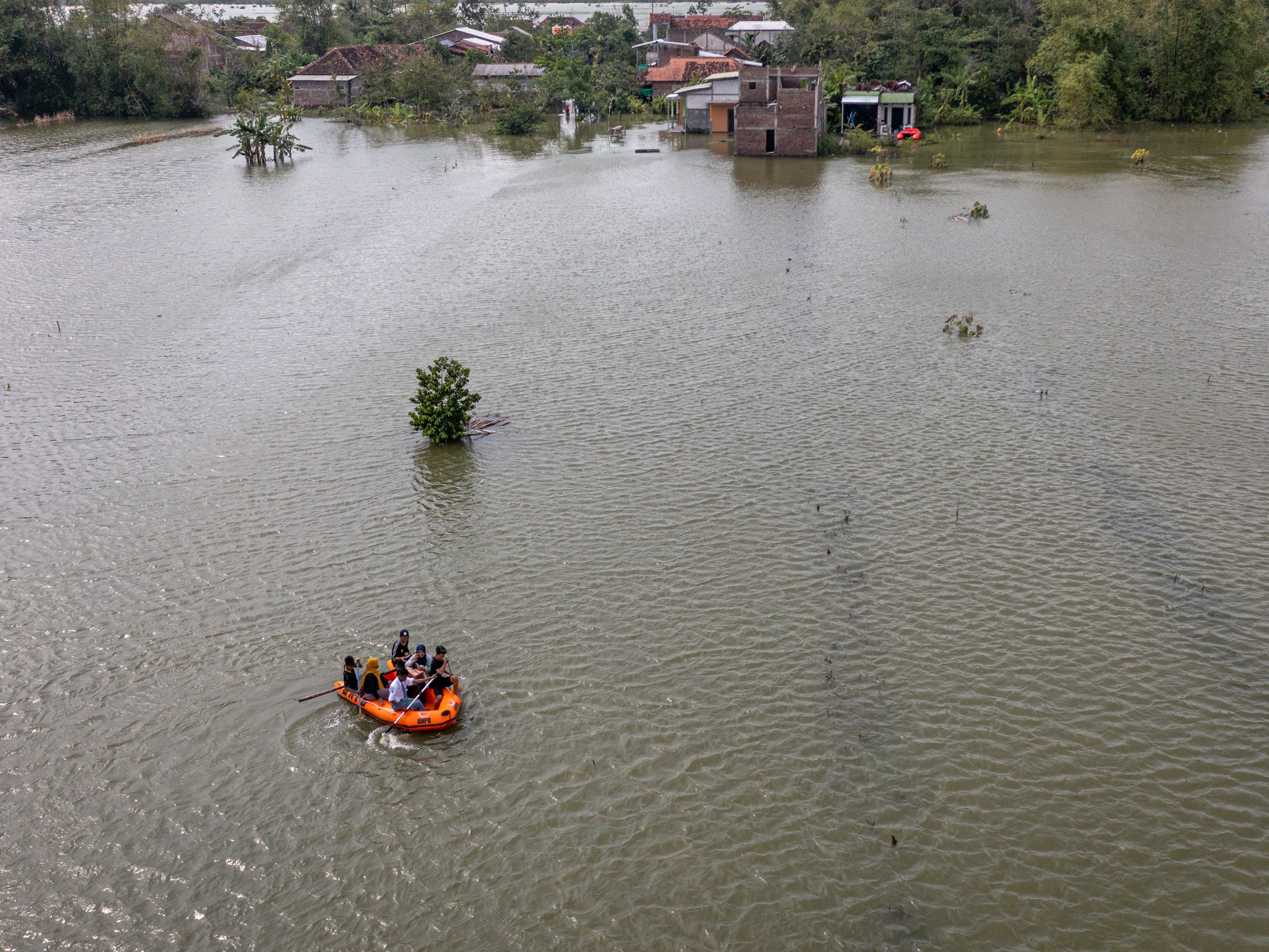 Foto udara sejumlah warga mendayung perahu karet di sekitar areal persawahan yang terendam banjir Di Desa Prampelan, Kecamatan Sayung.