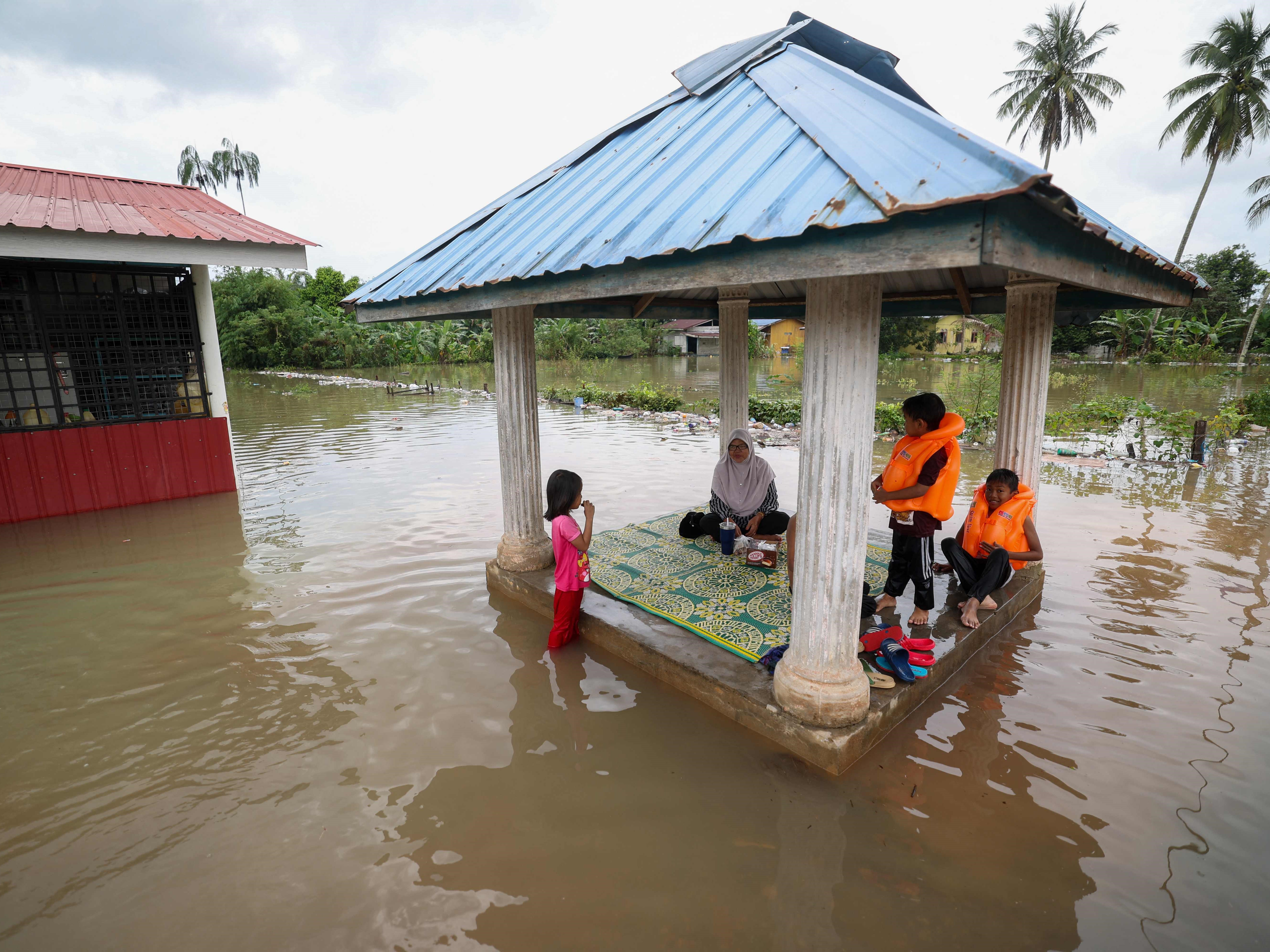 Satu keluarga duduk di pergola yang dikelilingi air banjir di Pasir Mas di negara bagian Kelantan utara Malaysia pada 21 Desember 2022. 