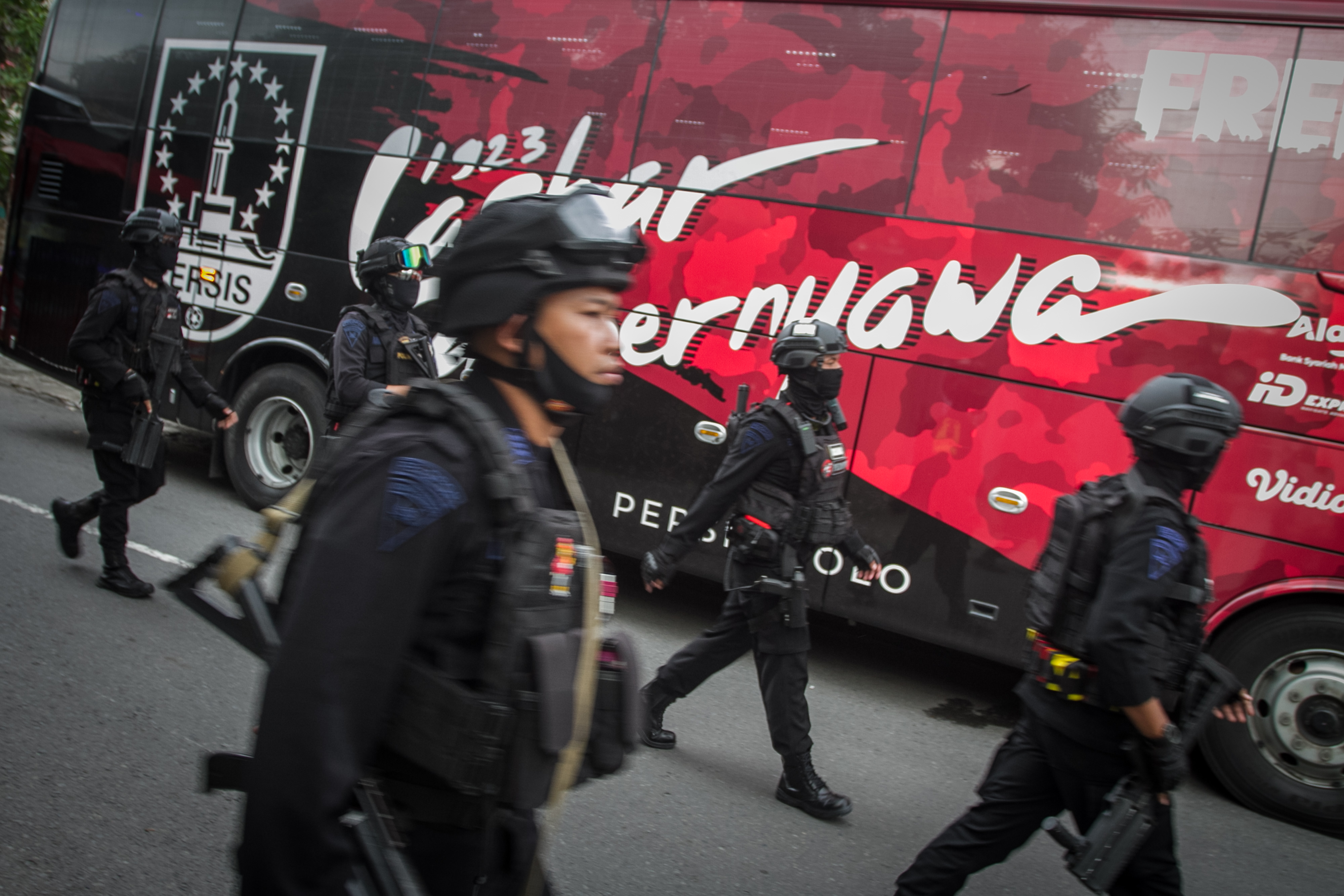 Petugas kepolisian berjalan di sekitar bus pemain sepak bola.