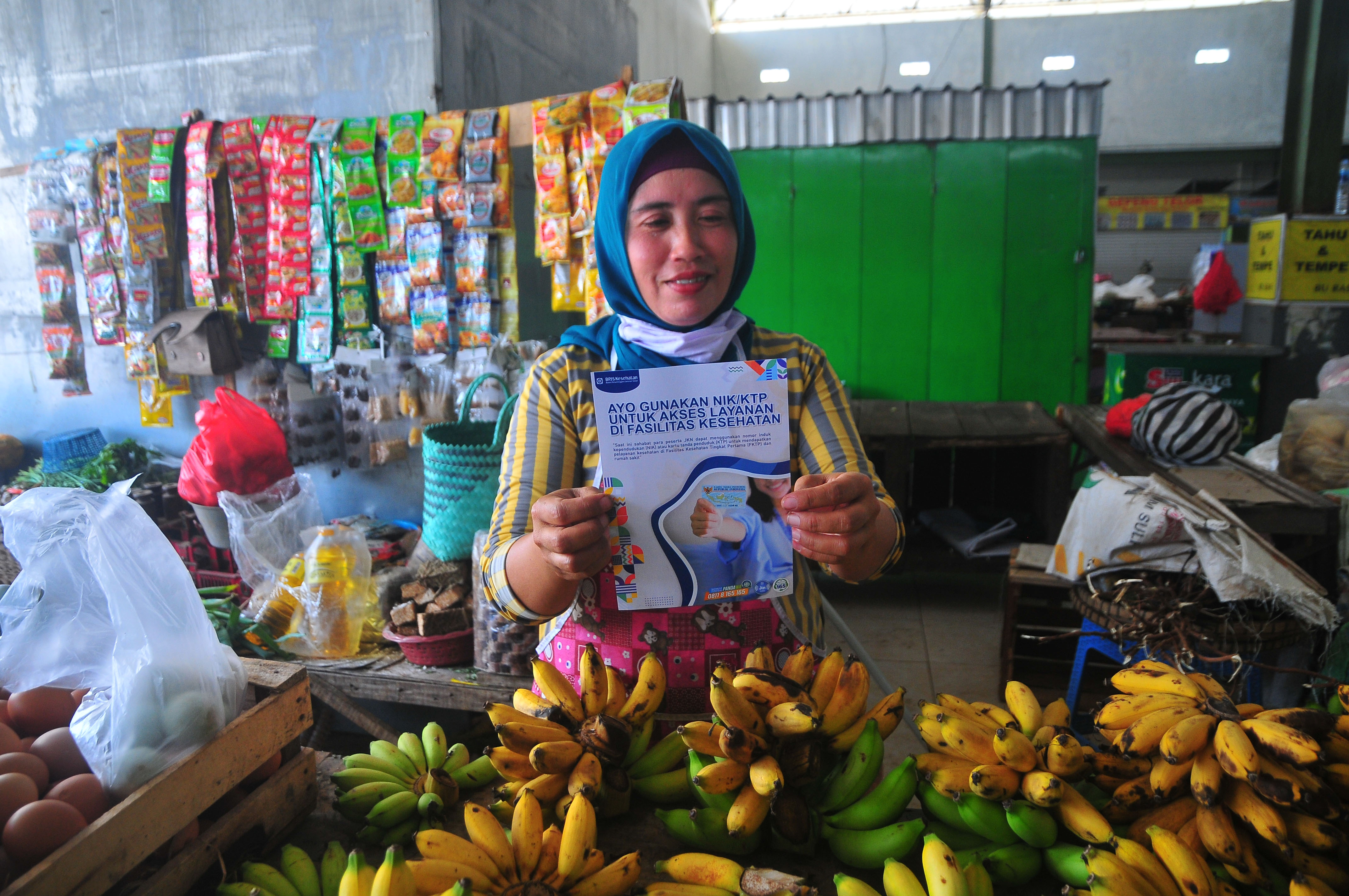 Pedagang memperlihatkan brosur Jaminan Kesehatan Nasional (JKN) di Pasar Rakyat, Kudus, Jawa Tengah, Selasa (30/8/2022)