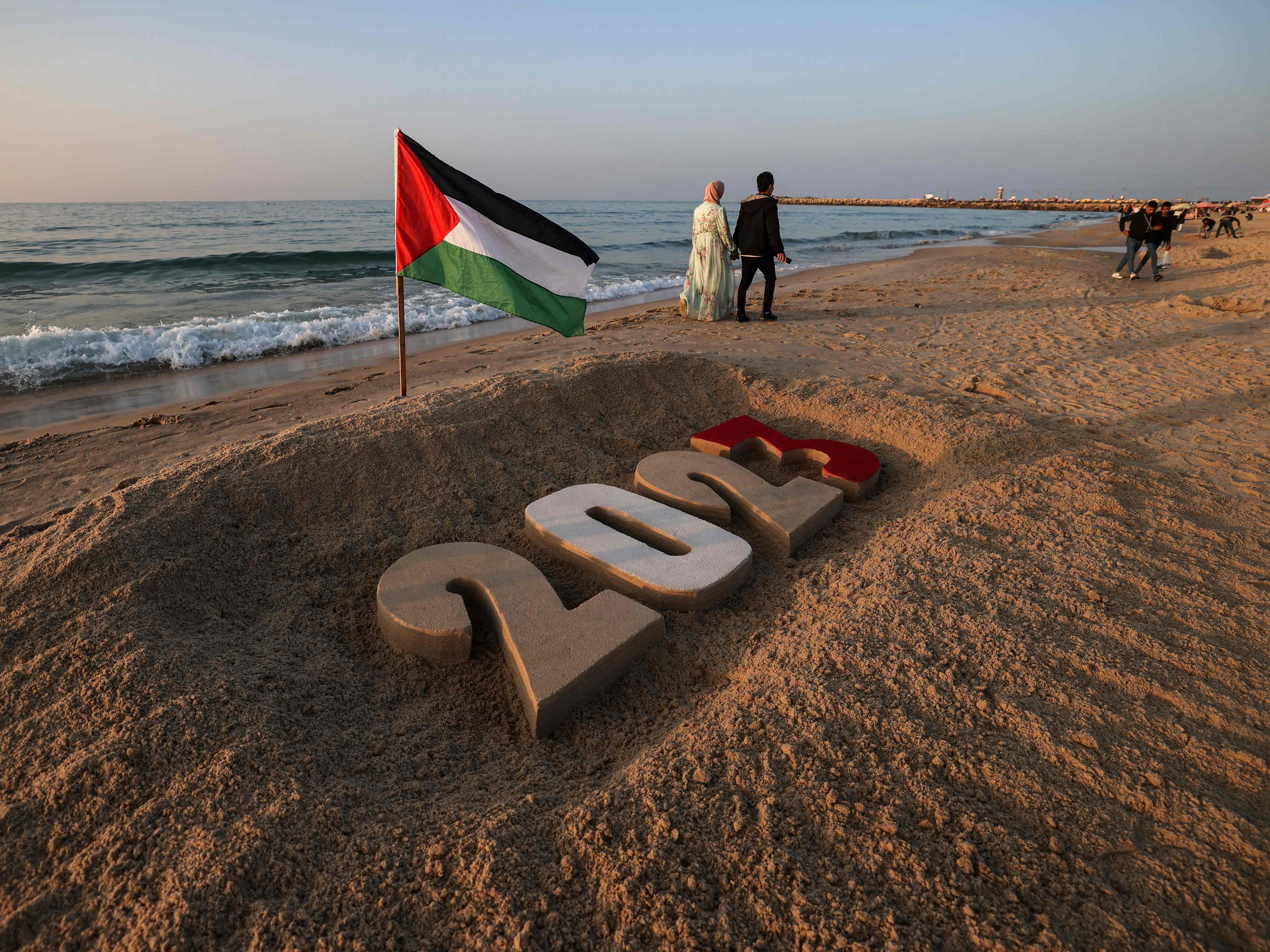 Warga Palestina berjalan melewati kreasi pasir bertuliskan 2023 di pantai, Kota Gaza, pada 31 Desember 2022.