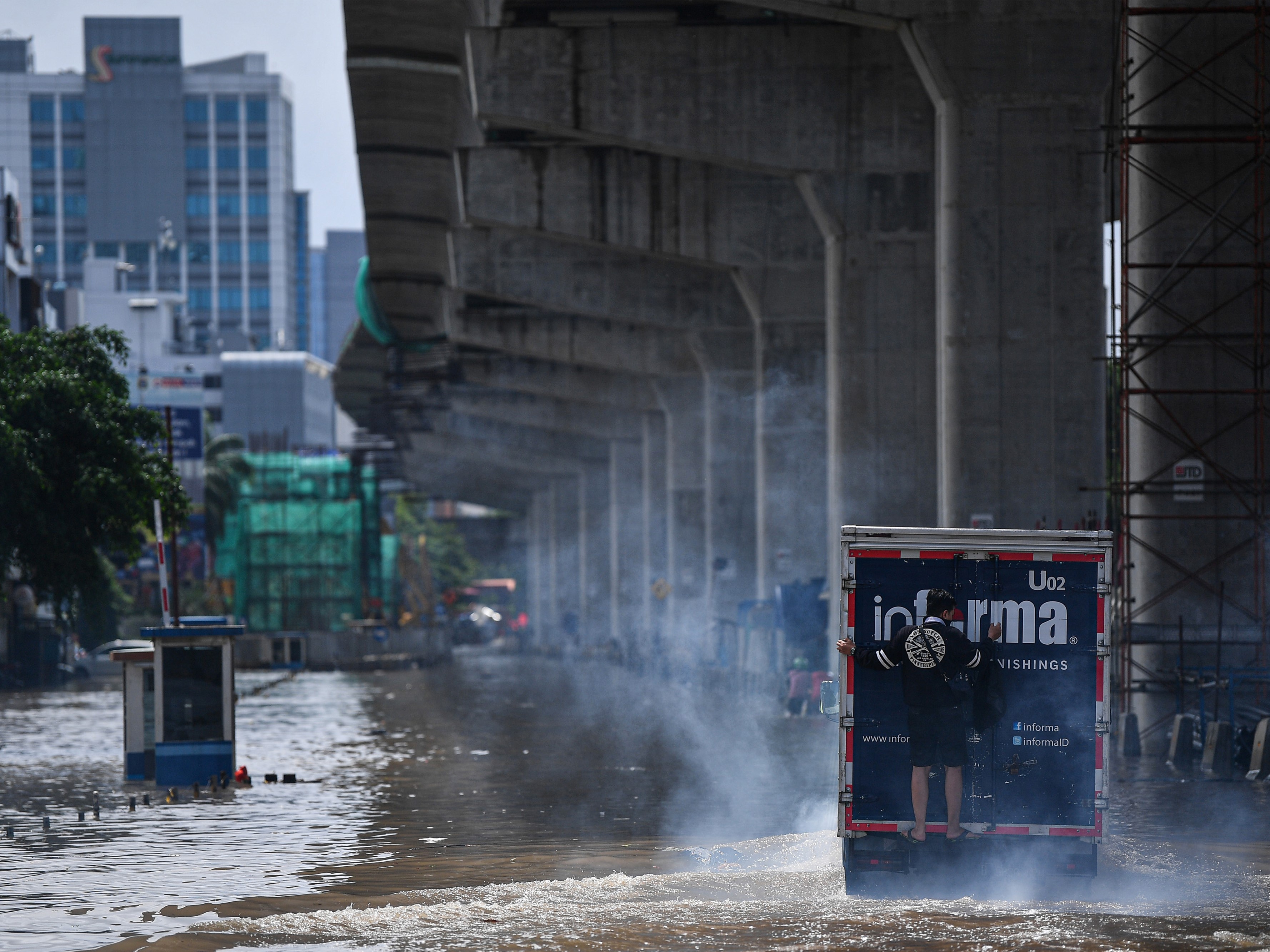 Seorang pria naik ke bagian belakang sebuah truk untuk melintasi banjir di Jalan Boulevard Barat Raya, Kelapa Gading, Jakarta Utara.