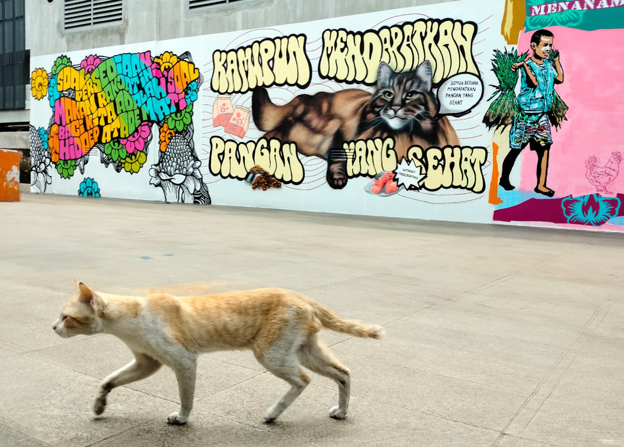 Seekor kucing melintas di dekat mural bertema daulat pangan di komplek Taman Ismail Marzuki (TIM), Jakarta Pusat.