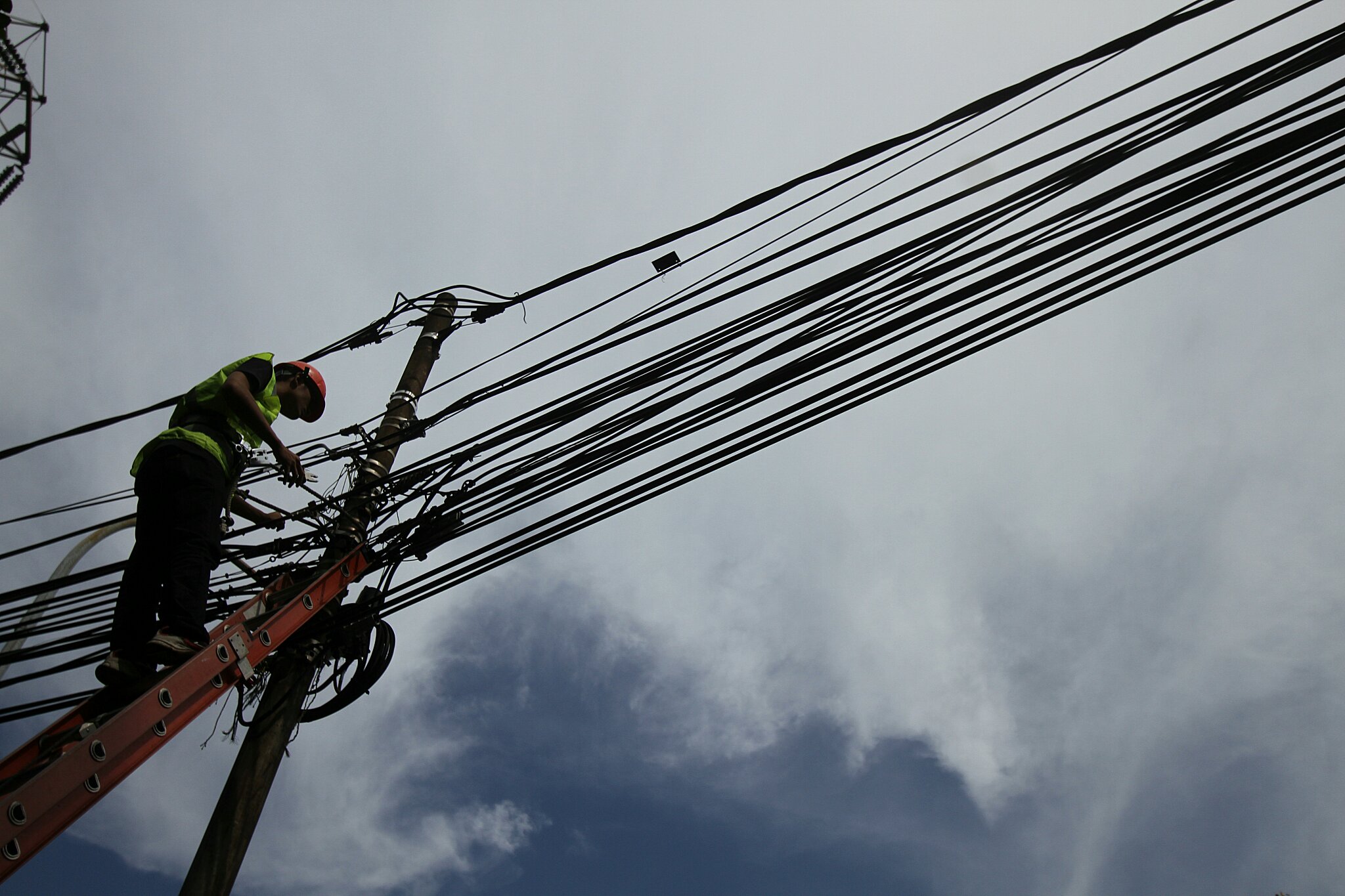 Potret petugas mengecek instalasi kabel di tiang listrik.