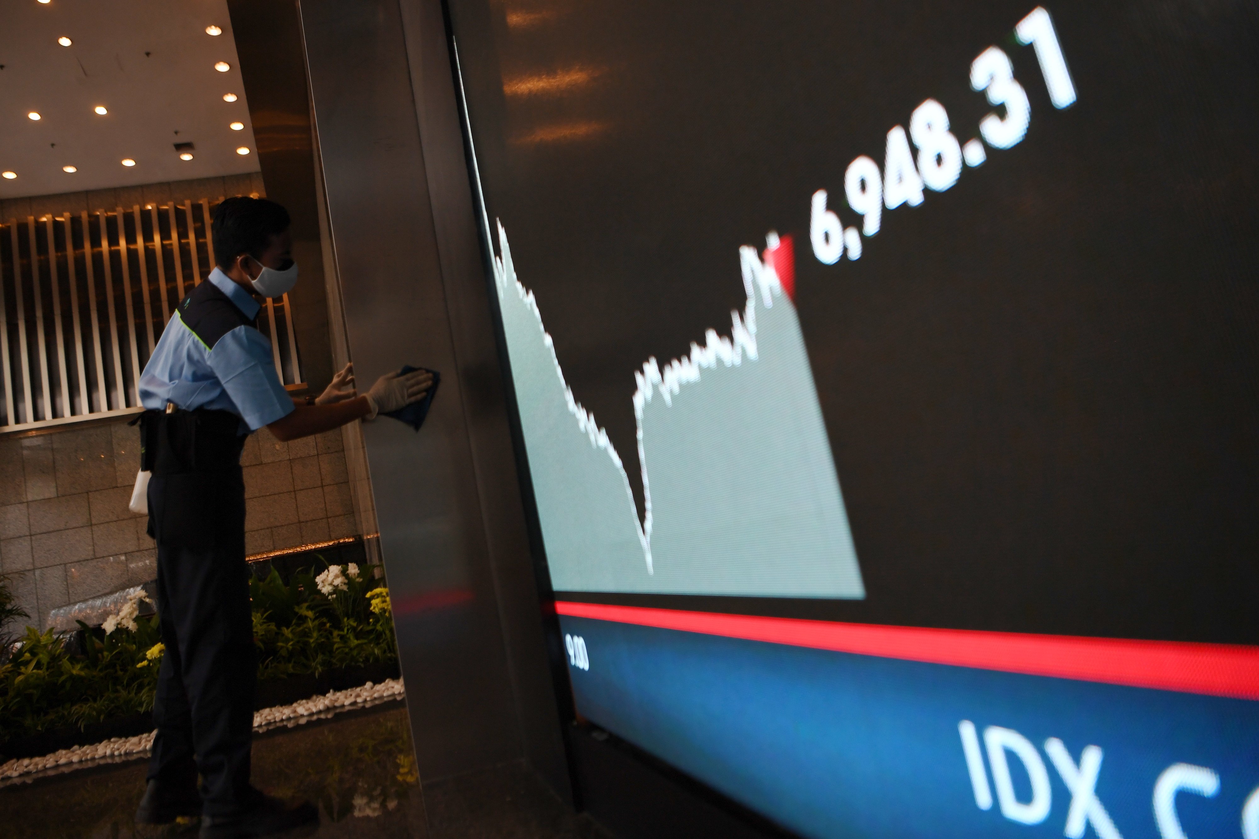 Pekerja membersihkan area di dekat layar pergerakan IHSG.