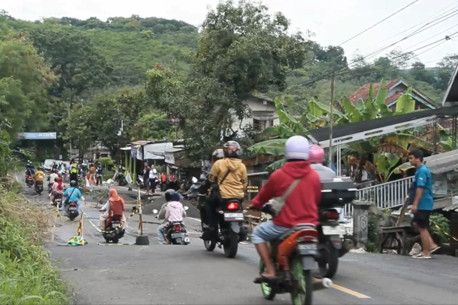 Pengendara sepeda motor melalui jalan yang ambles.