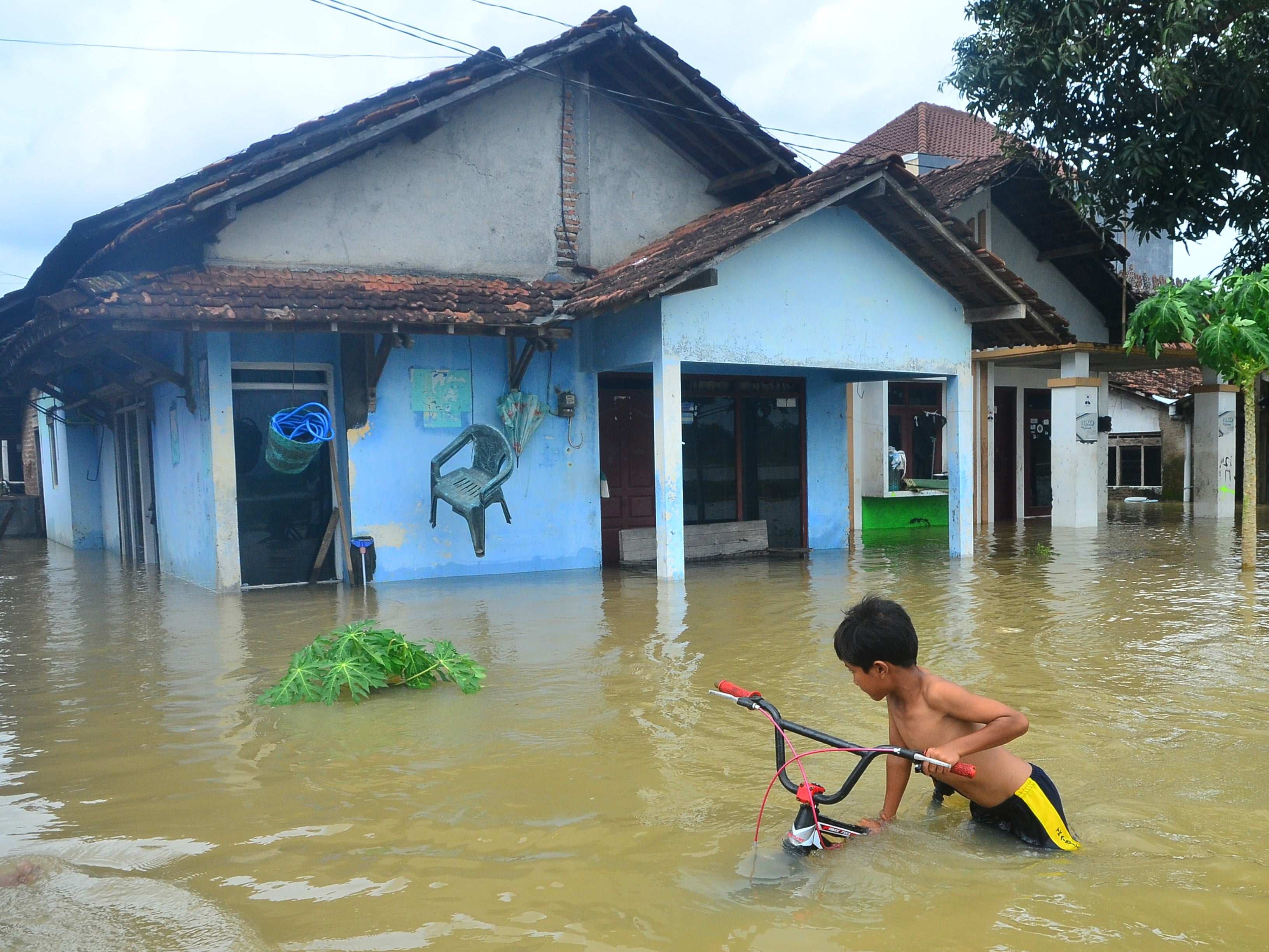 Seorang anak menuntun sepeda melewati jalan yang terendam banjir di Desa Temulus, Mejobo, Kudus, Jawa Tengah, Minggu (1/1/2023).