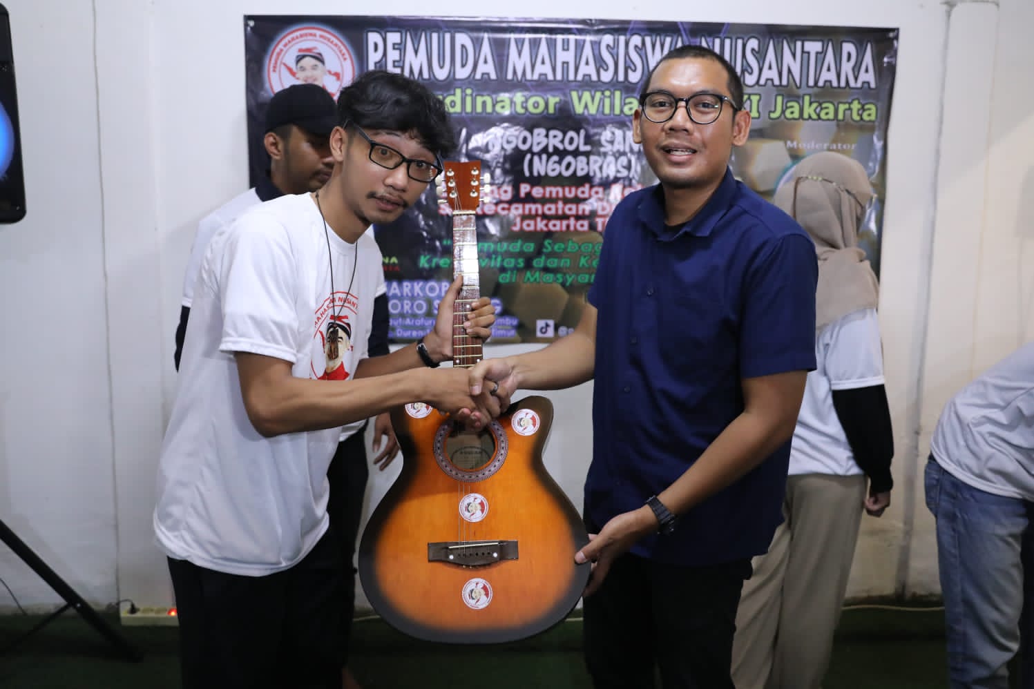Koordinator Wilayah PMN DKI Jakarta Tiba Yuda Laksana (kaos biru) menyerahkan bantuan alat musik gitar kepada anak muda di Kecamatan Duren S