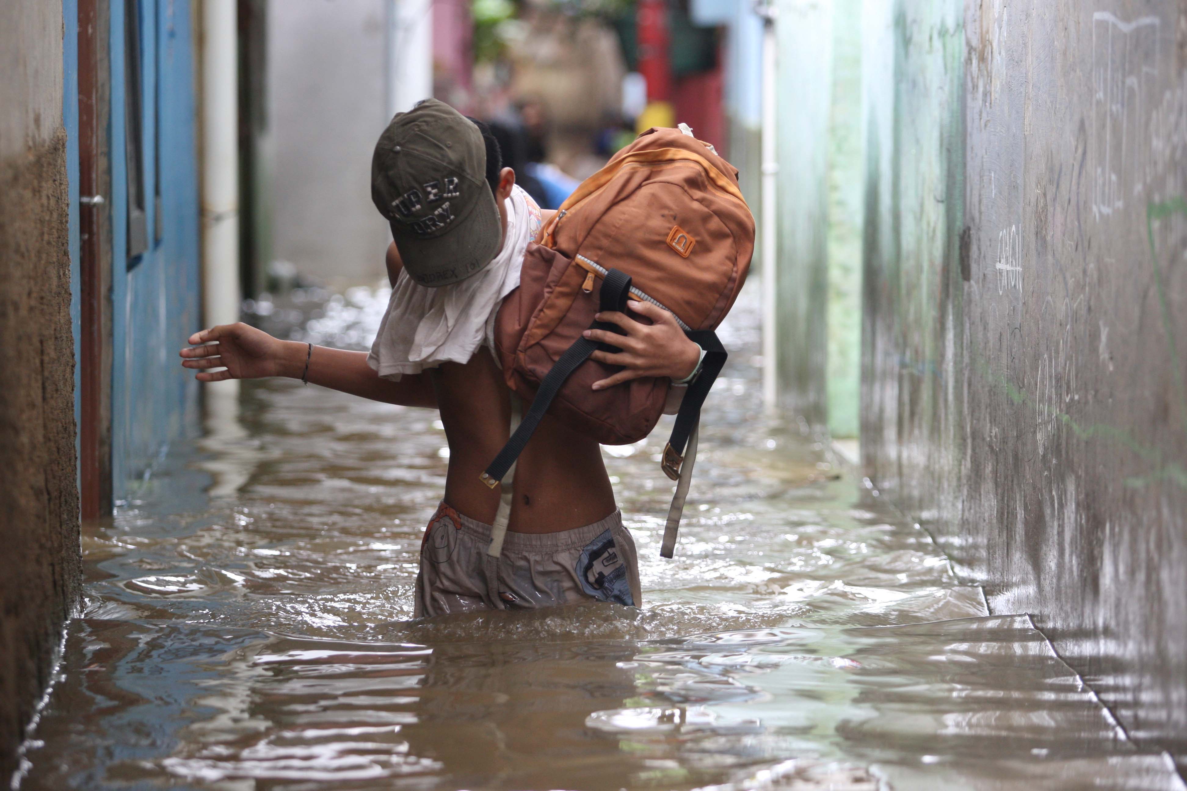 Warga beraktivitas di tengah banjir yang mengepung RT 13/RW 04, Kebon Pala, Kecamatan Jatinegara, Jakarta Timur, Senin (27/02/2023).