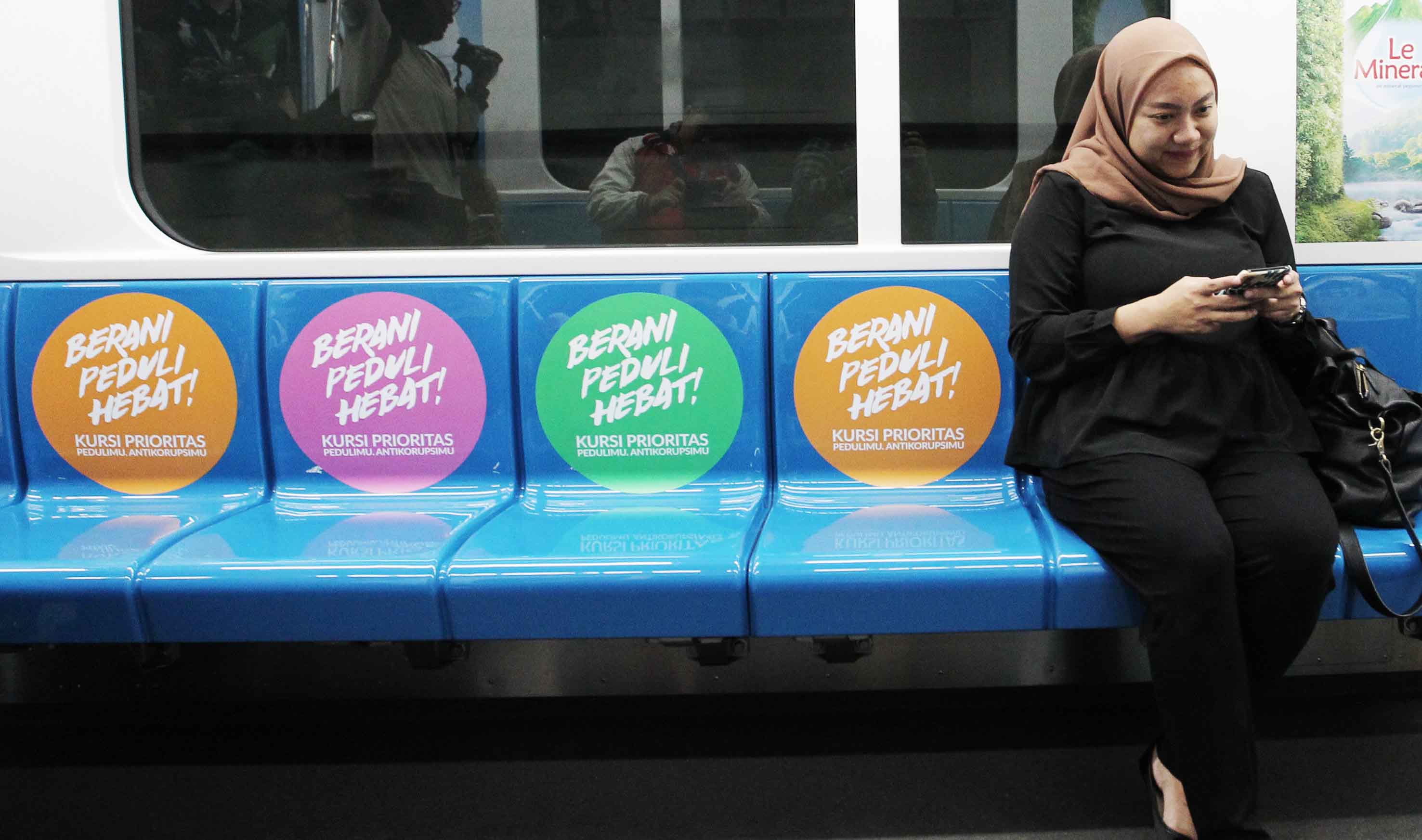 Penumpang duduk dikursi yang sudah ditempel stiker kampanye anti korupsi di gerbong kereta MRT