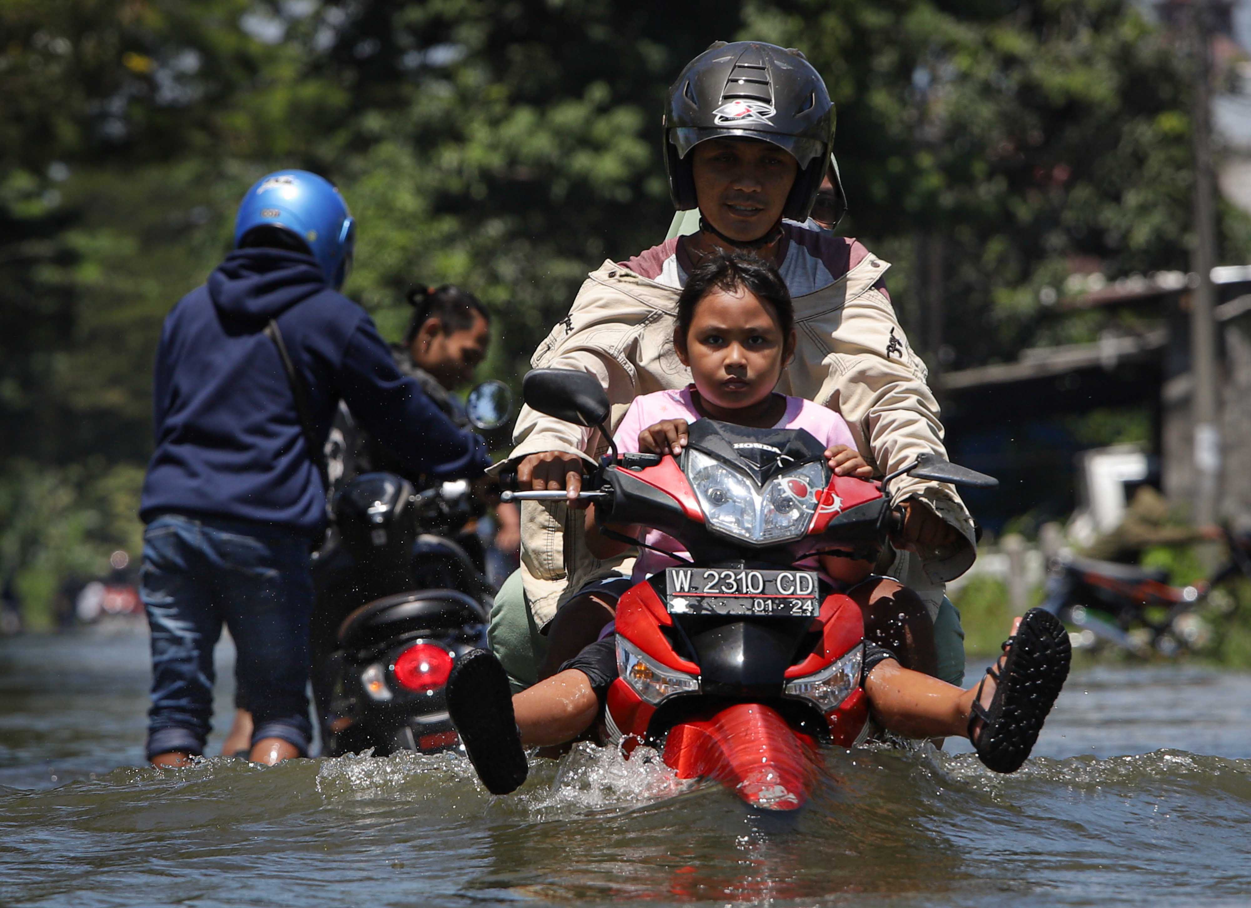 Pengendara sepedsa motor melintasi jalan yang tergenang banjir di Jalan Raya Morowudi, Gresik, Jawa Timur, Senin (20/2).