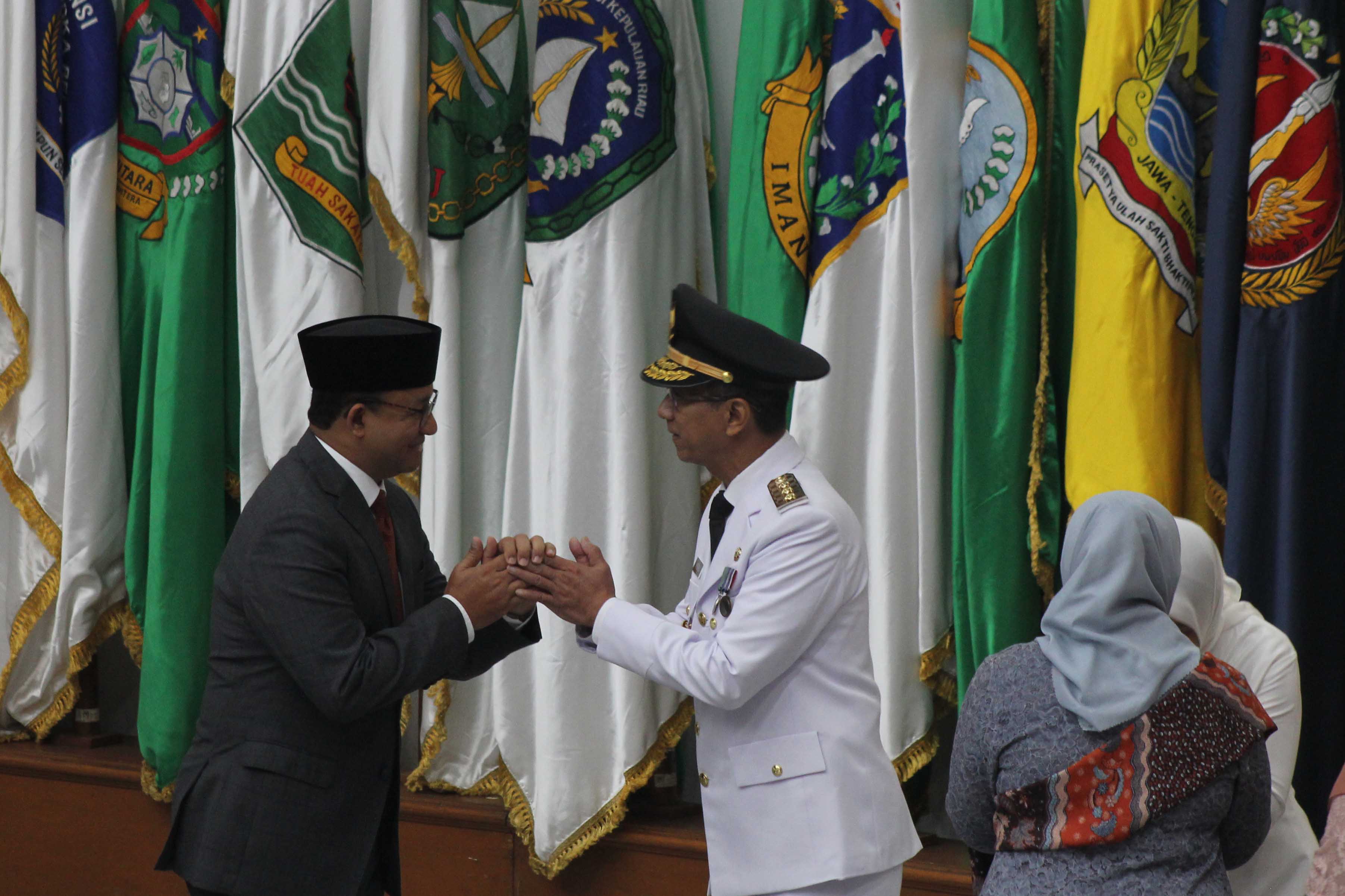 Pj Gubernur DKI Jakarta Heru Budi Hartono berjabat tangan dengan Anies Baswedan.