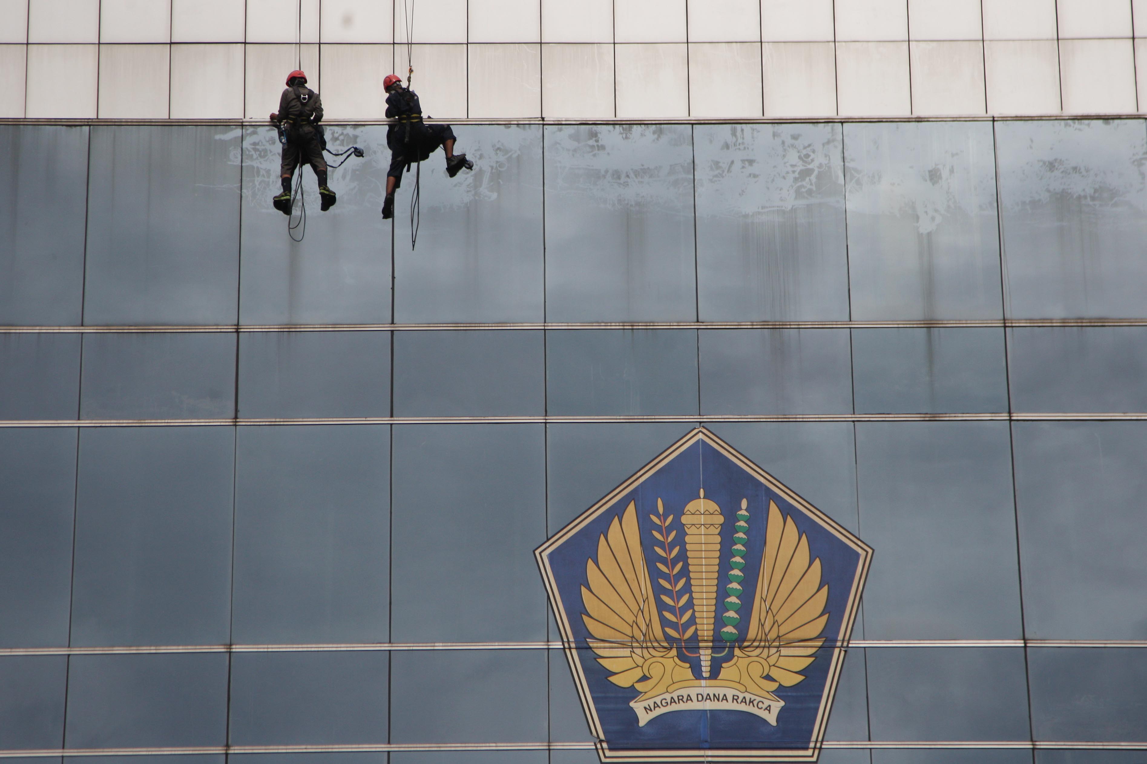 Petugas membersihkan kaca di gedung kantor pelayanan Ditjen Pajak wilayah Jakarta.