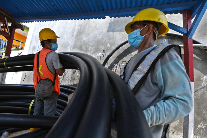 Pekerja Perumda Perusahaan Air Minum (PAM) Jaya mengangkat pipa air bersih untuk dipasang di Kamal Muara, Jakarta.