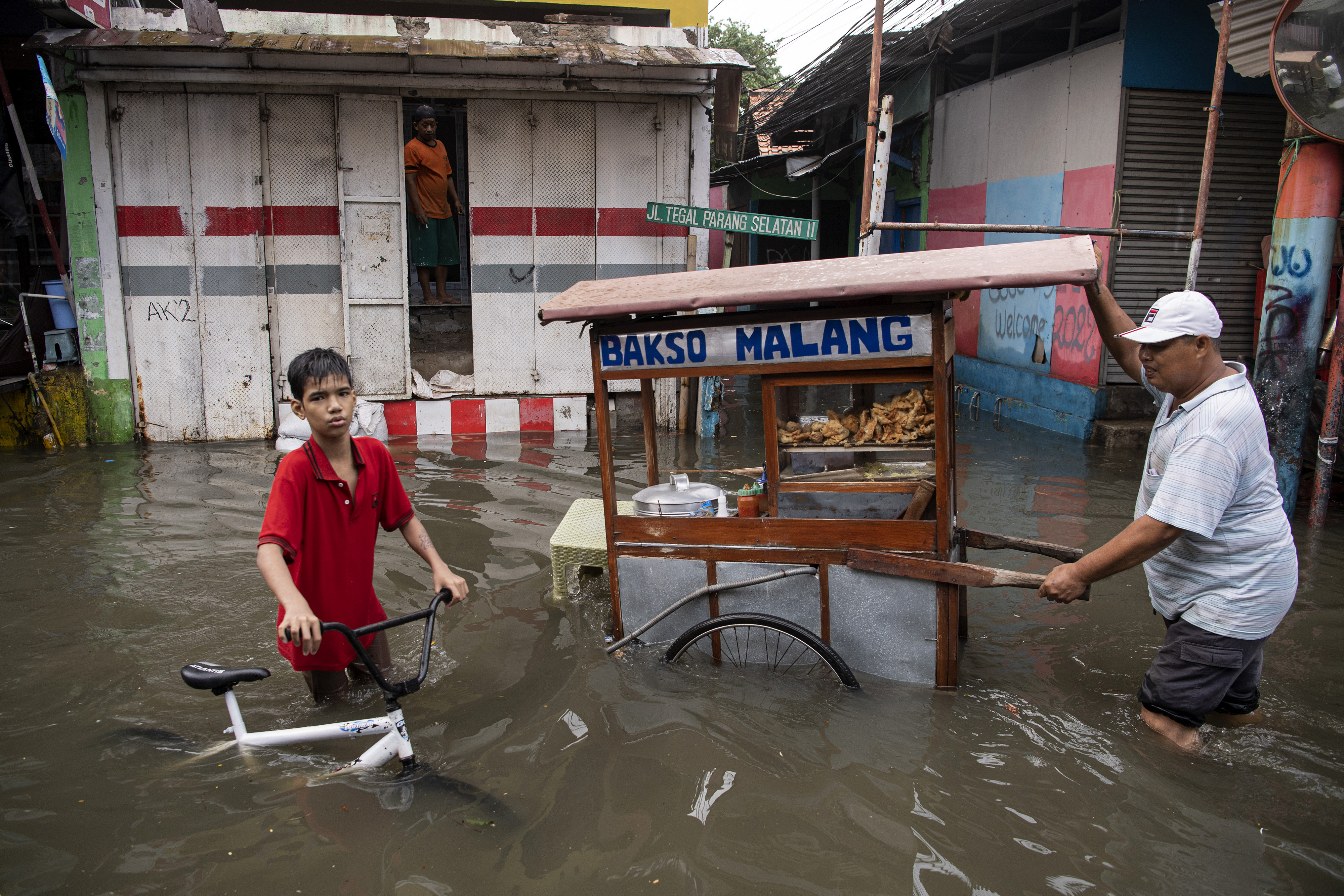 Pedagang bakso dan seorang anak dengan sepedanya melintasi banjir di Tegal Parang, Jakarta Selatan,  Sabtu (5/11/2022).