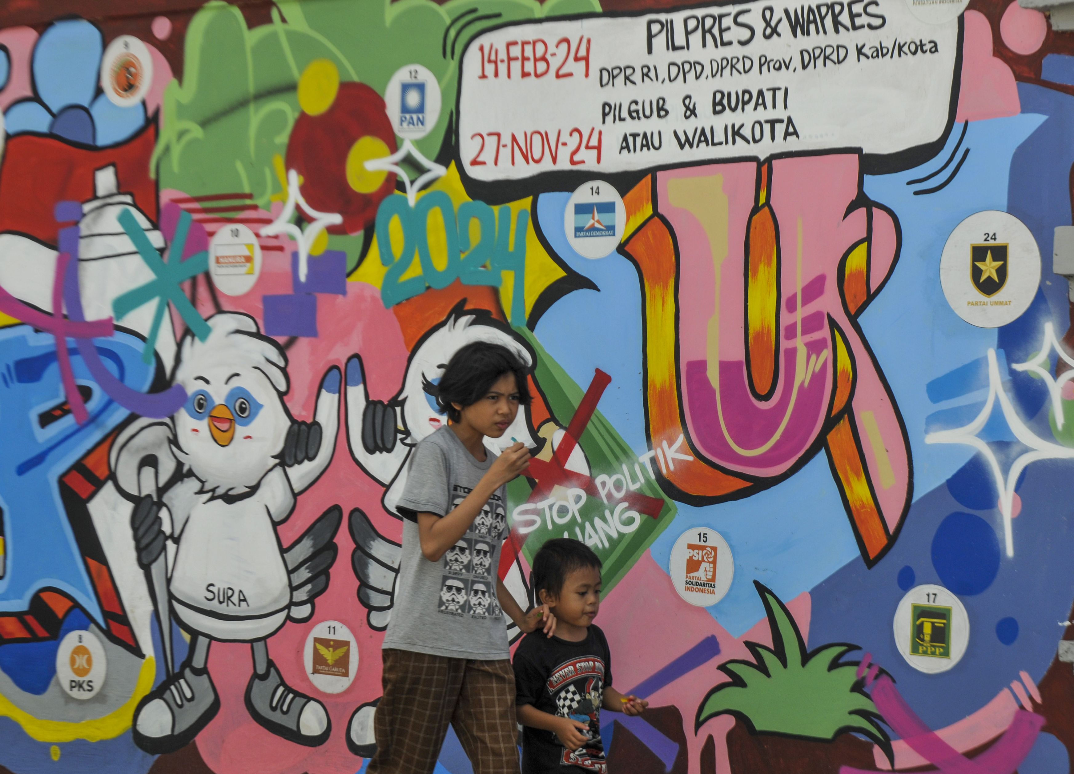 Dua anak berjalan melintasi mural Pemilu 2024 di Pandeglang