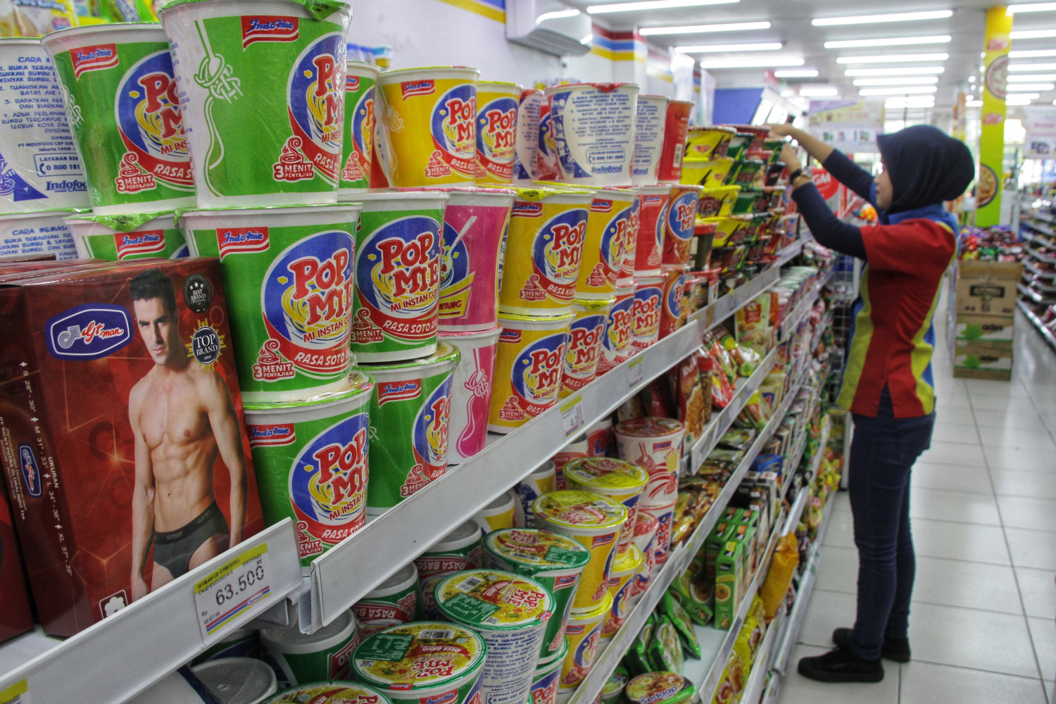 Seorang pegawai merapikan makanan instan di rak sebuah minimarket di Jakarta.