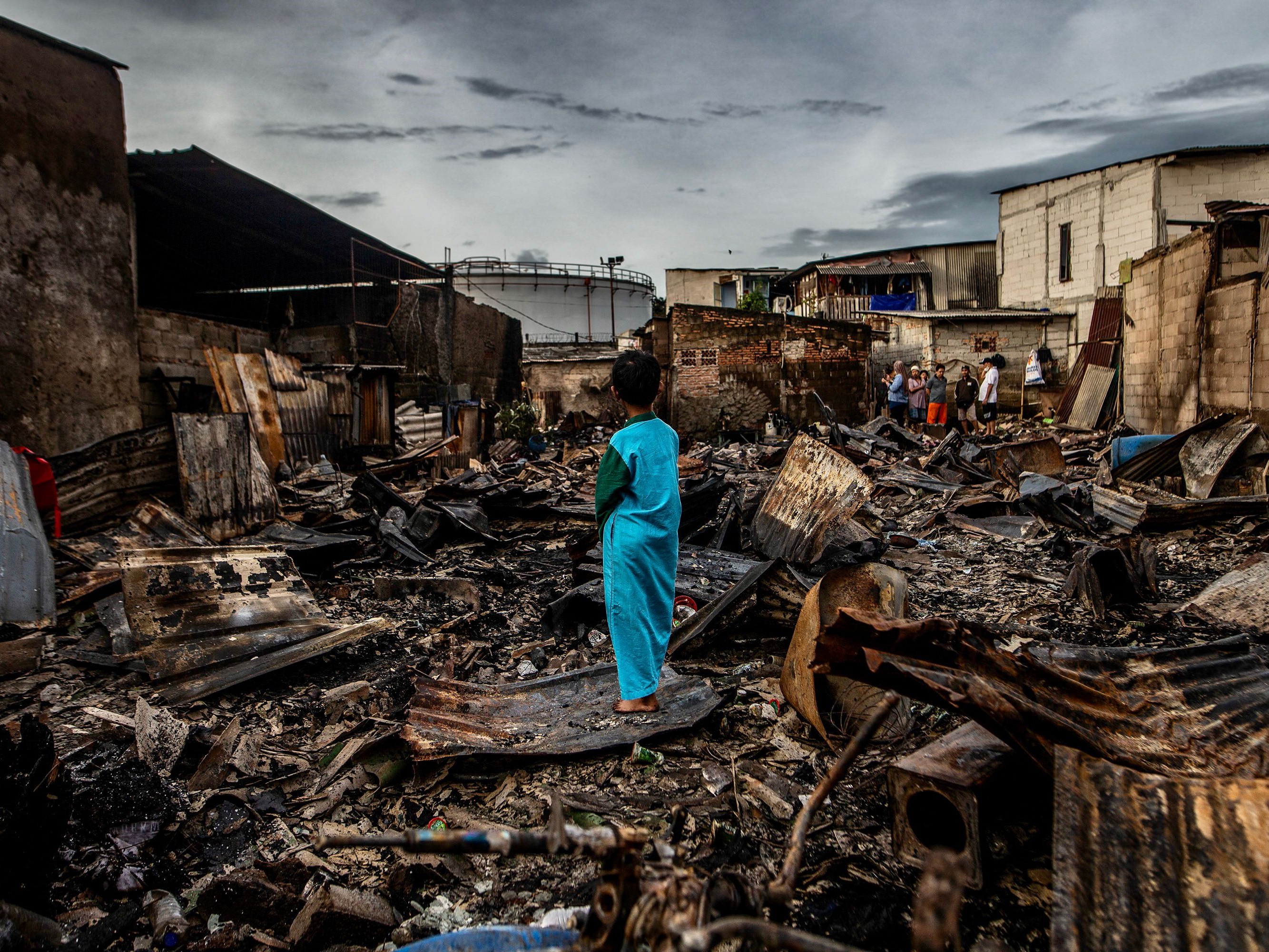 Seorang anak laki-laki berdiri di sisa-sisa rumah yang terbakar di daerah perumahan di Plumpang, Jakarta Utara, pada 4 Maret 2023.