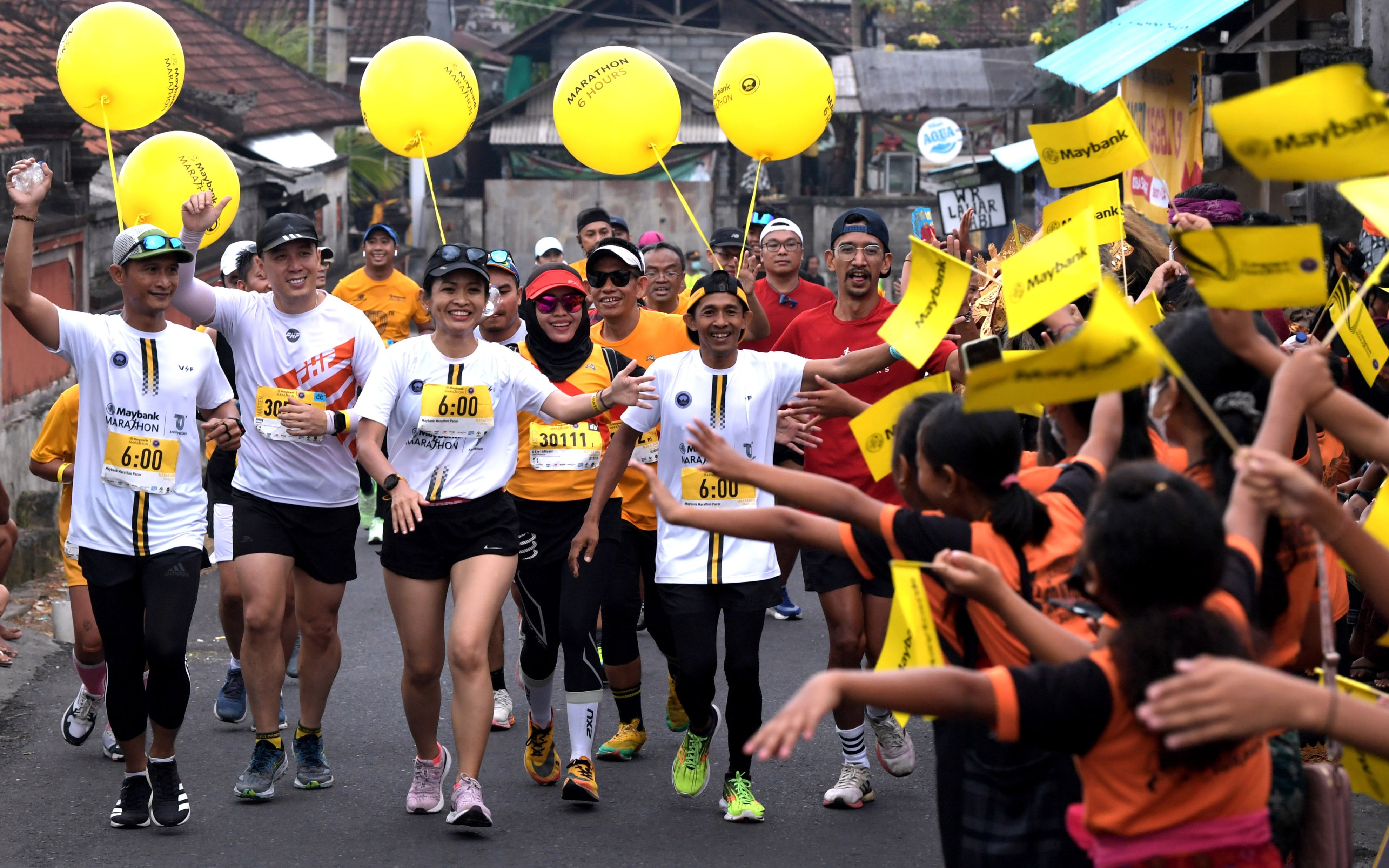 Peserta menyapa anak-anak saat mengikuti nomor kategori maraton pada Maybank Marathon 2022 di kawasan Gianyar, Bali, Minggu (28/8/2022).