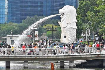 Para turis berfoto dengan latar belakang patung kepala singa bertubuh ikan yang merupakan maskot negara Singapura di Taman Merlion.