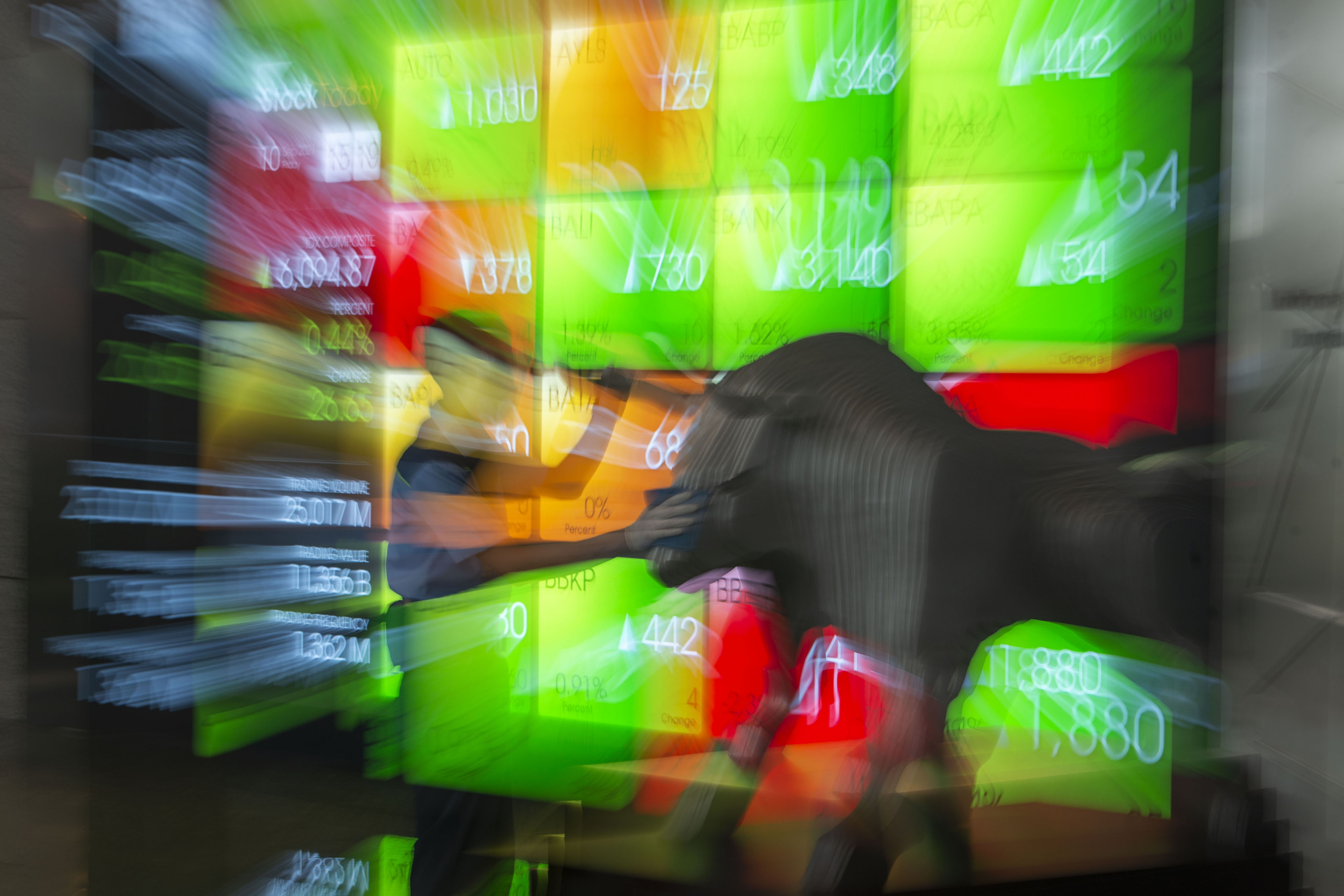 Pekerja membersihkan patung banteng dengan latar belakang layar pergerakan Indeks Harga Saham Gabungan (IHSG).