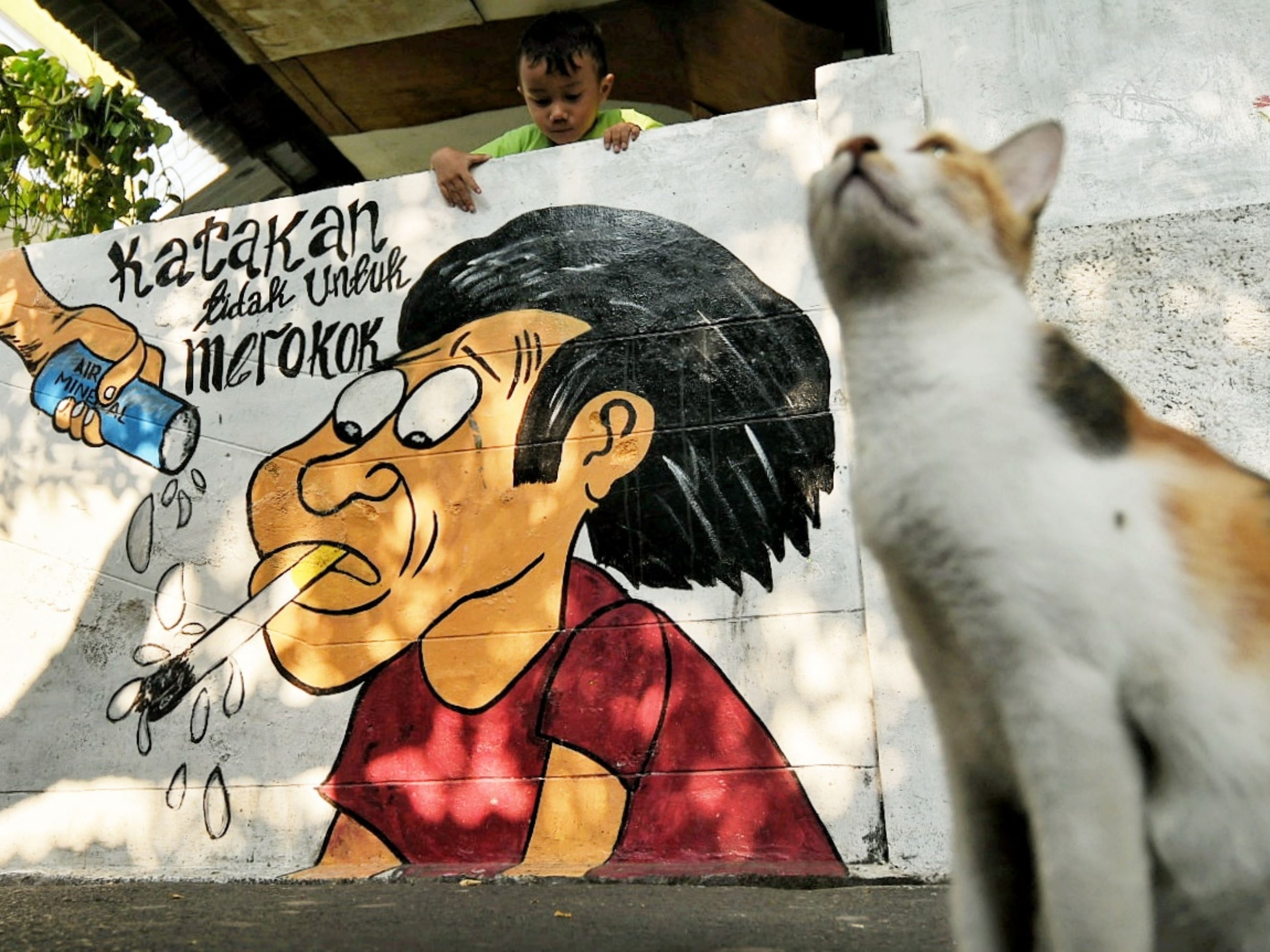 Warga beraktivitas dekat mural bertema kawasan bebas asap rokok di lingkungan RW 06 Kelurahan Kayu Manis, Matraman, Jakarta.