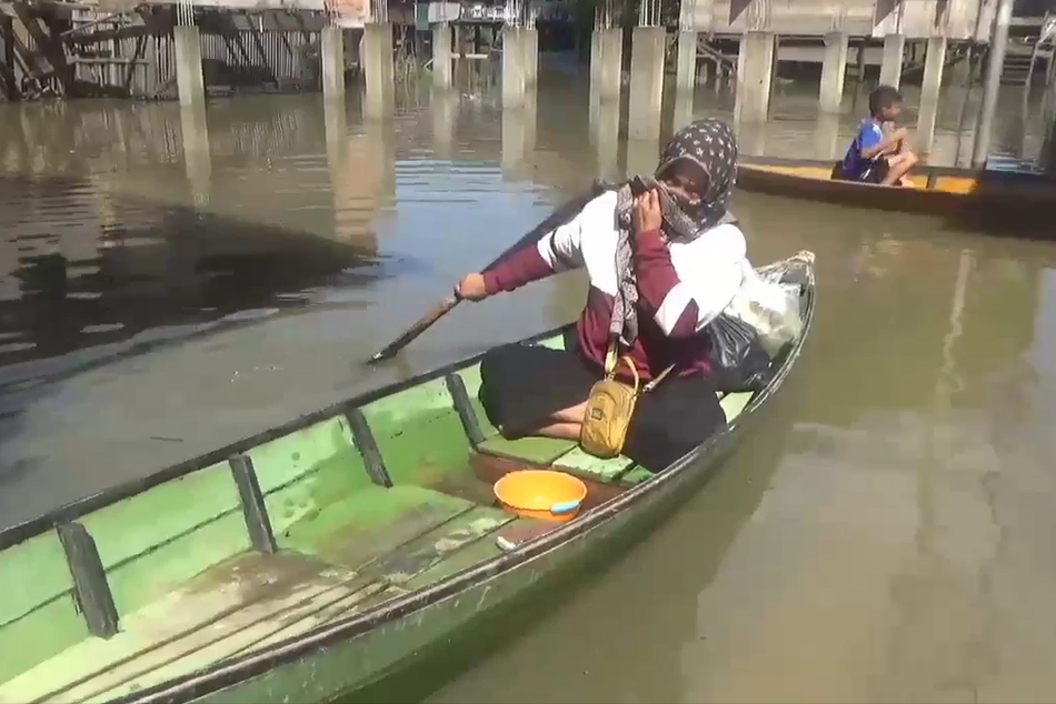 Warga menggunakan perahu karena banjir menggenangi daerahnya.