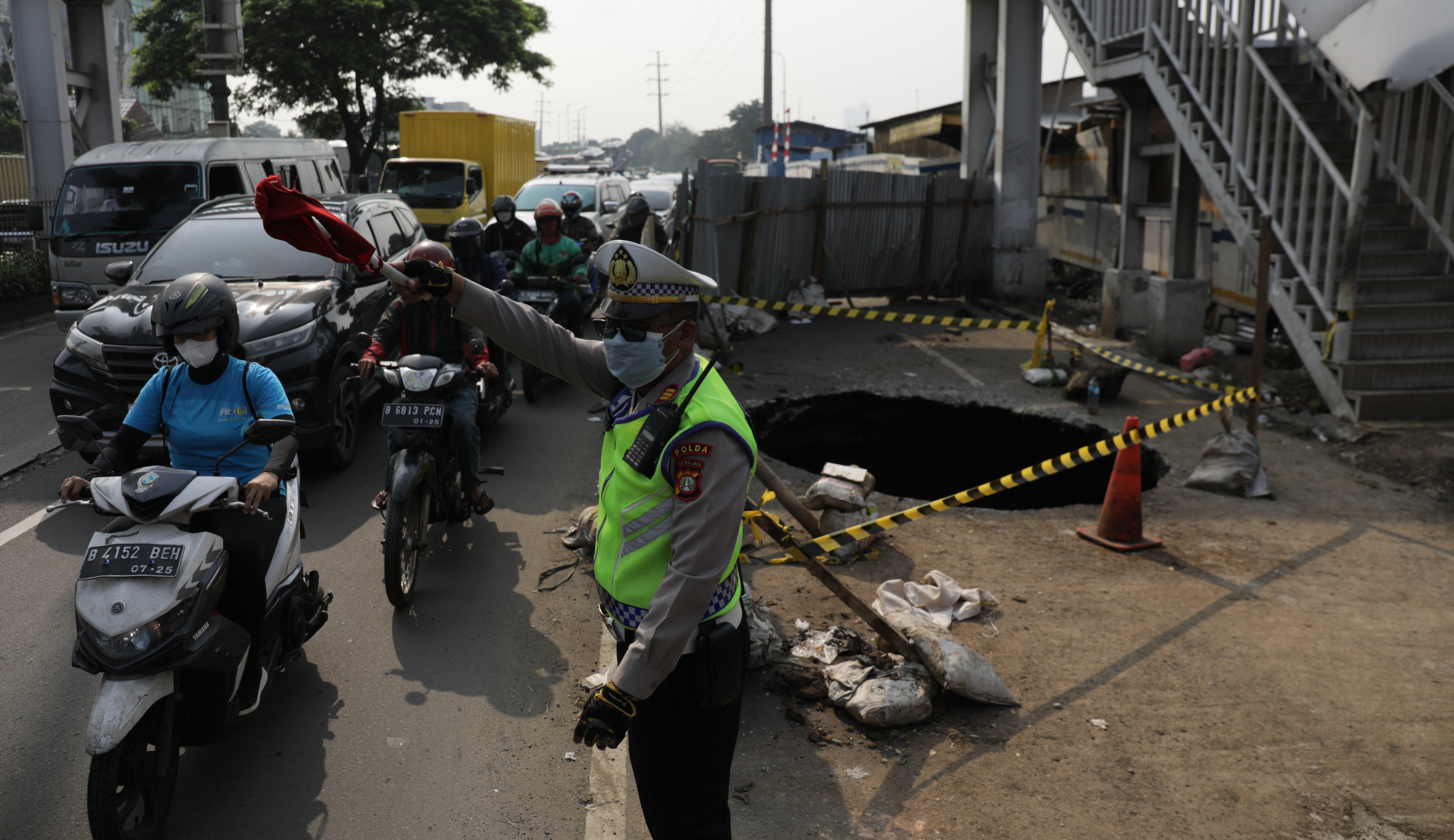 Polisi mengatur arus lalu lintas di dekat lokasi Jalan amblas membentuk lubang besar di Jalan Raya Daan Mogot, Jakarta Barat, Jakarta.