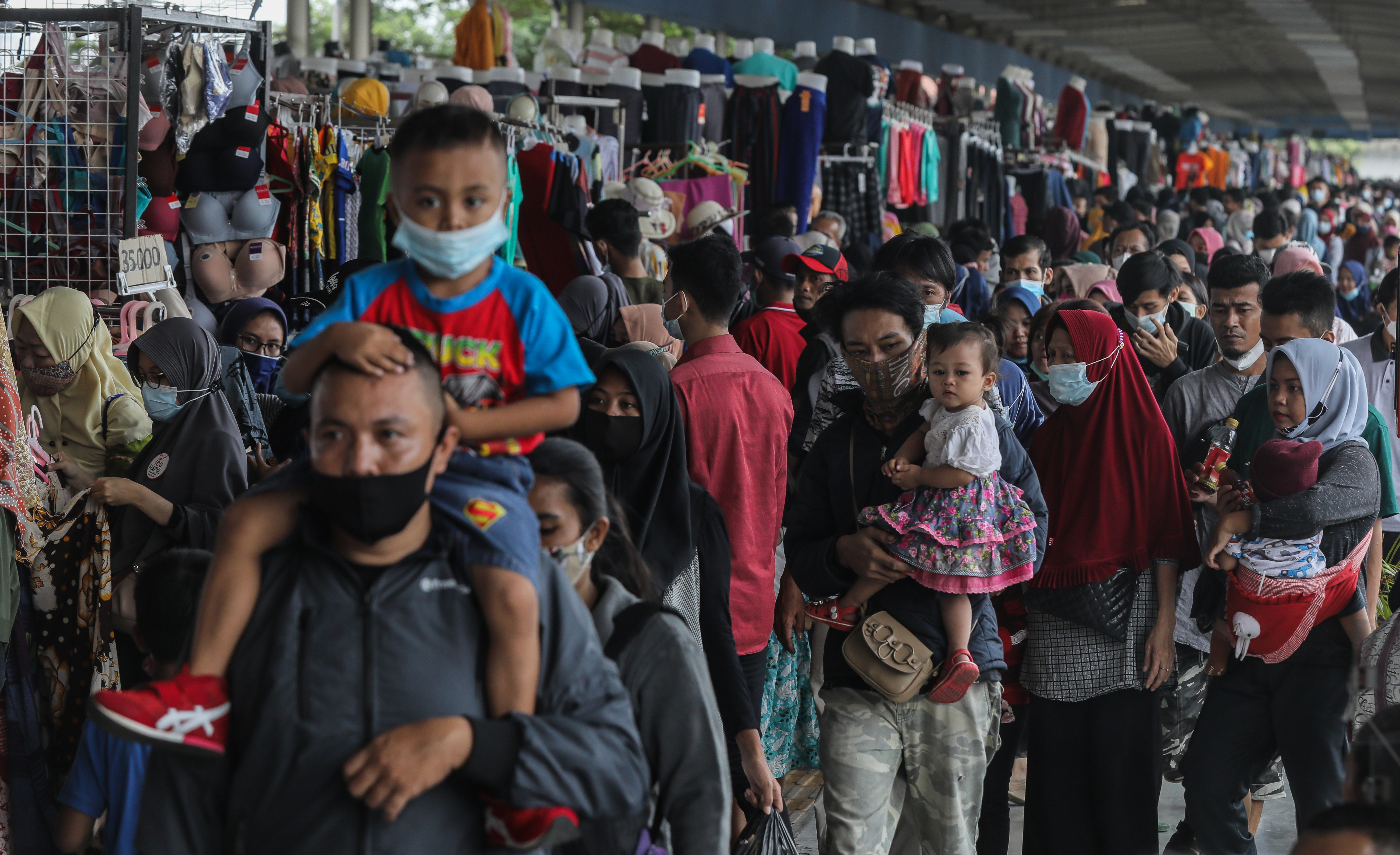 Pengunjung menggendong anaknya tanpa masker saat melewati kerumunan Sky Bridge Pasar Tanah Abang, Jakarta Pusat.