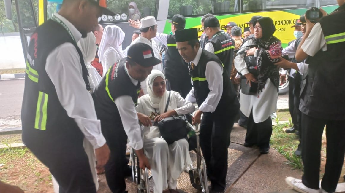 Petugas haji daerah kerja Madinah membantu jemaah lansia turun dari bus dalam simulasi pelayanan di Asrama Haji Pondok Gede, Jakarta.