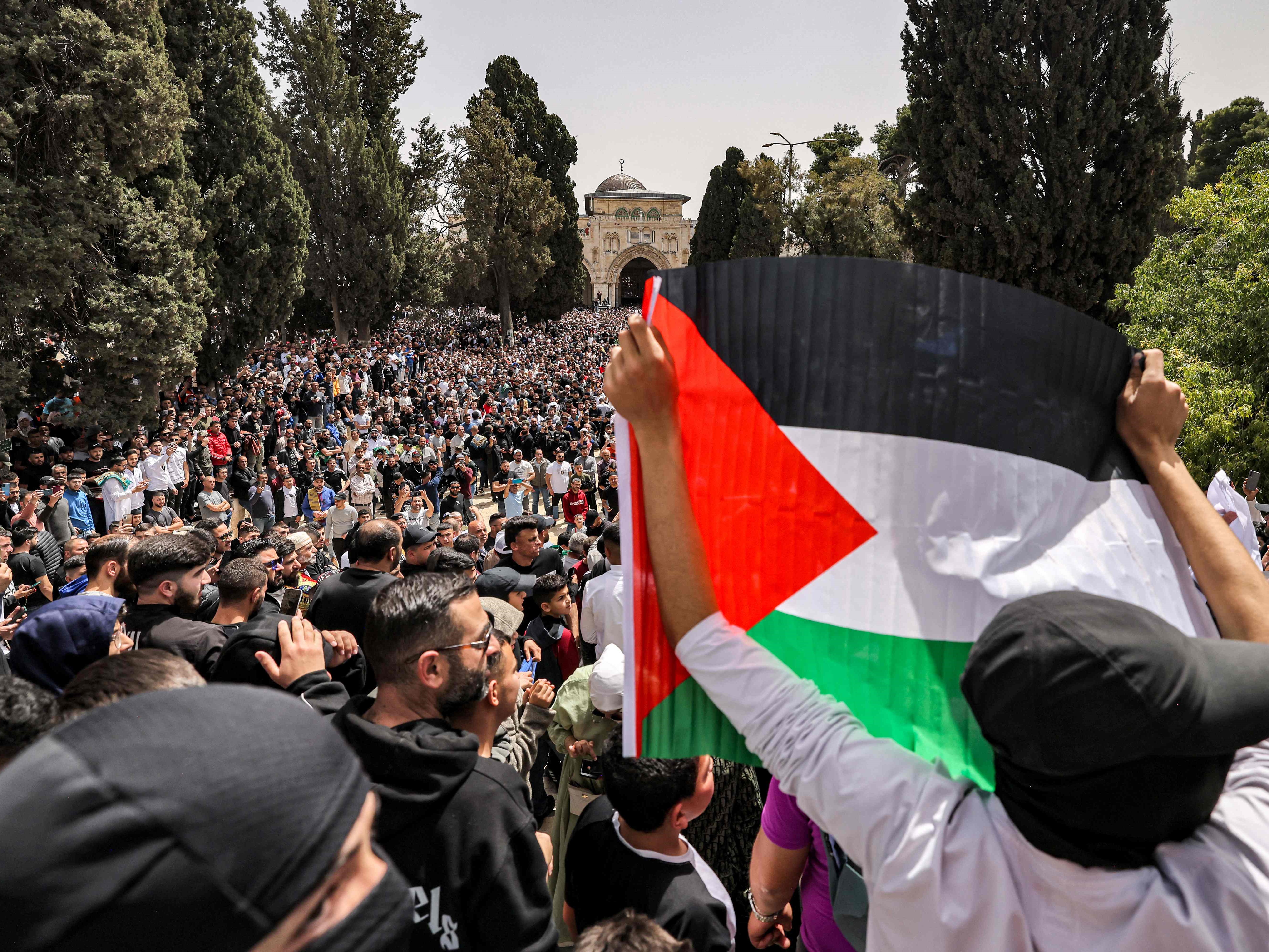 Seorang pria mengangkat kertas bendera Palestina di depan Masjid Al-Aqsa.