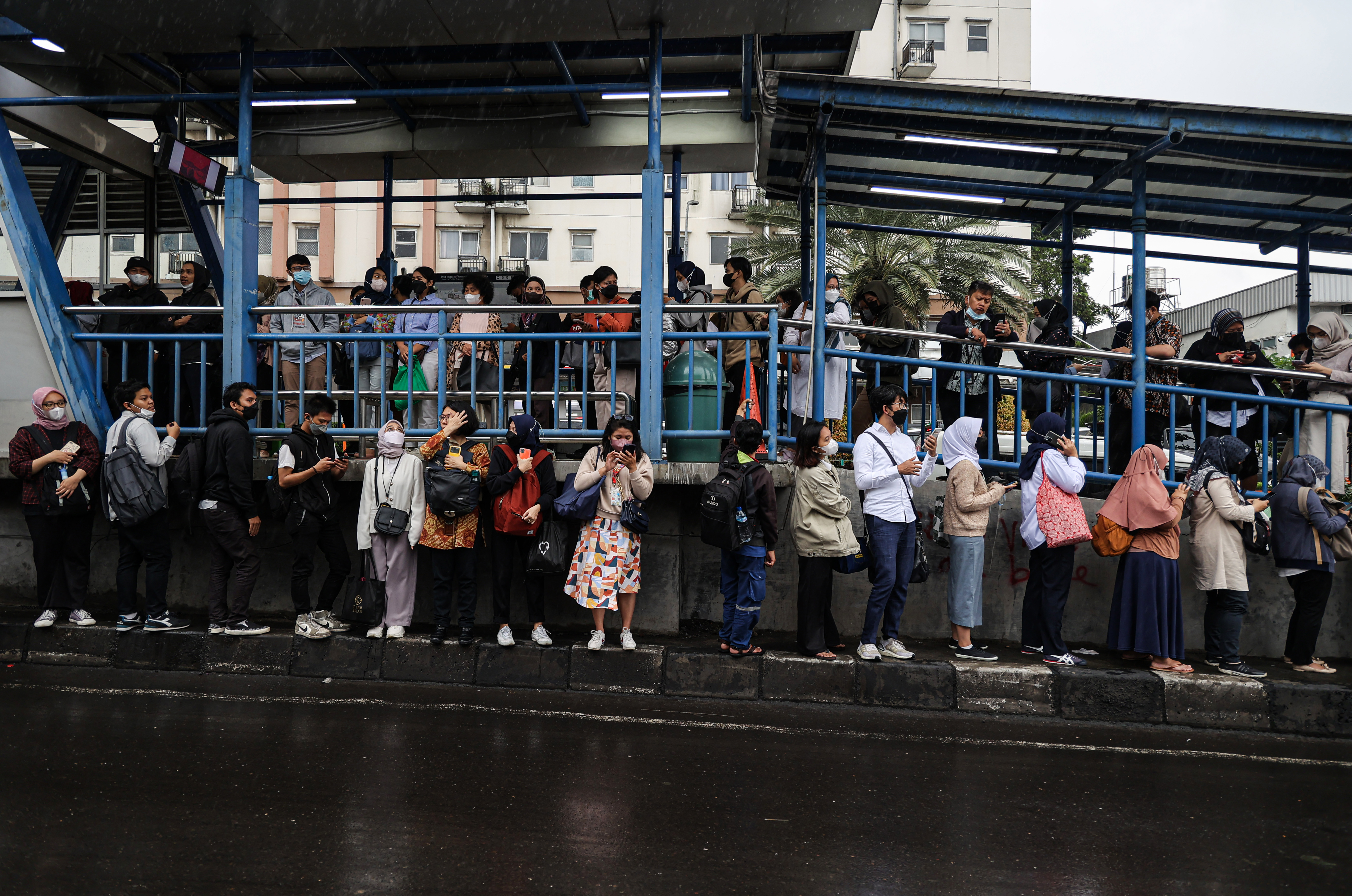 Calon penumpang bus TransJakarta antre hingga ke tepi jalan menunggu bus di Halte Bus Adam Malik, Jakarta Selatan, Senin (27/2/2023)