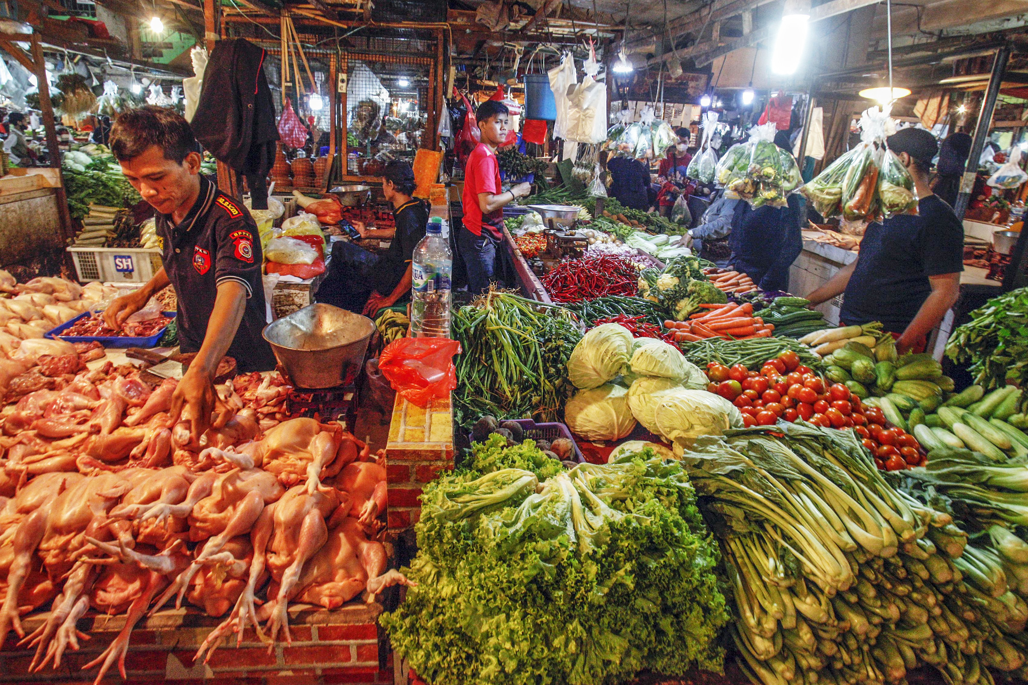  Pedagang ayam potong dan sayur mayur melayani pembeli di sebuah pasar.