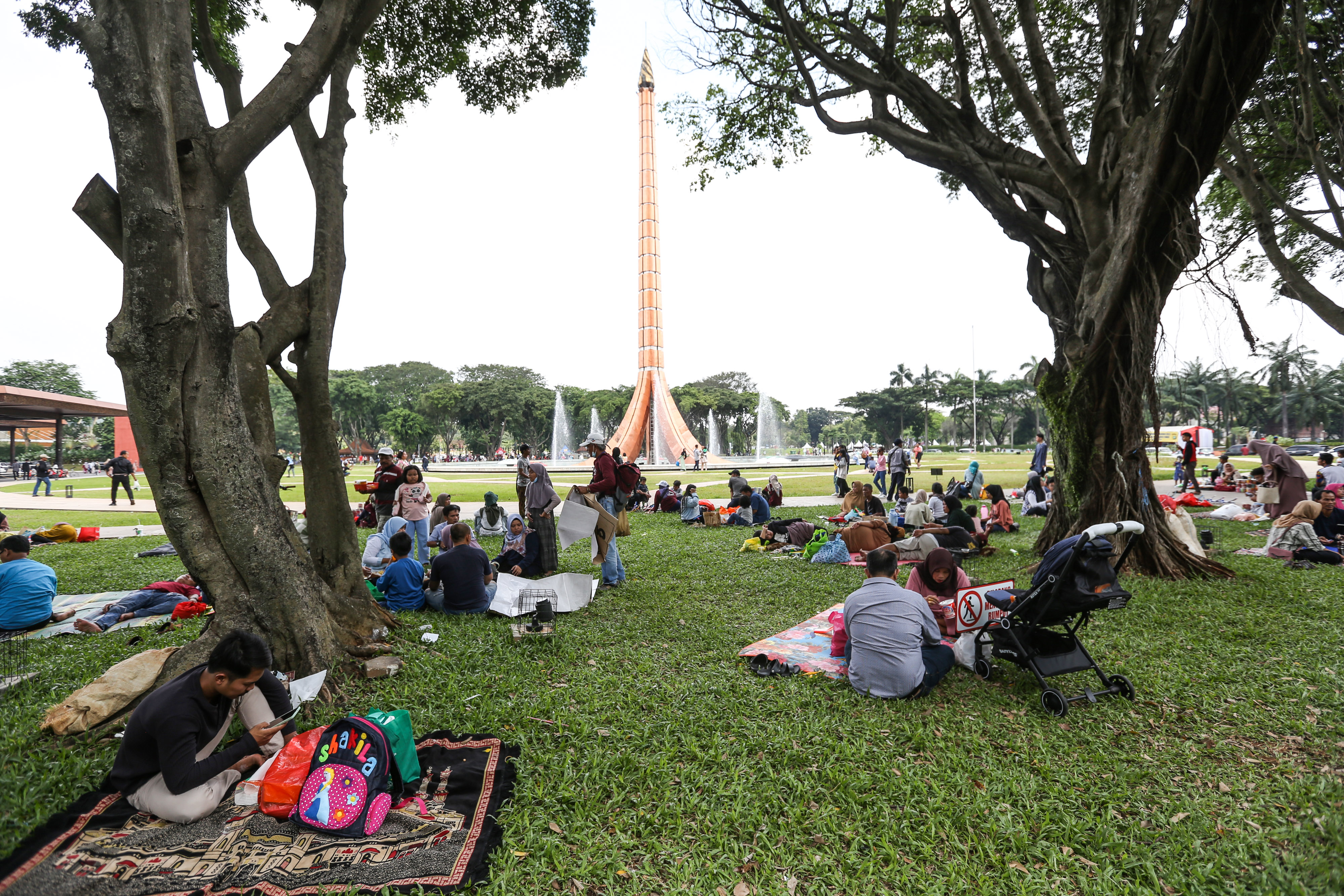 Sejumlah pengunjung bersantai di pinggir Tugu Api Taman Mini Indonesia Indah (TMII), Jakarta, Minggu (23/4).