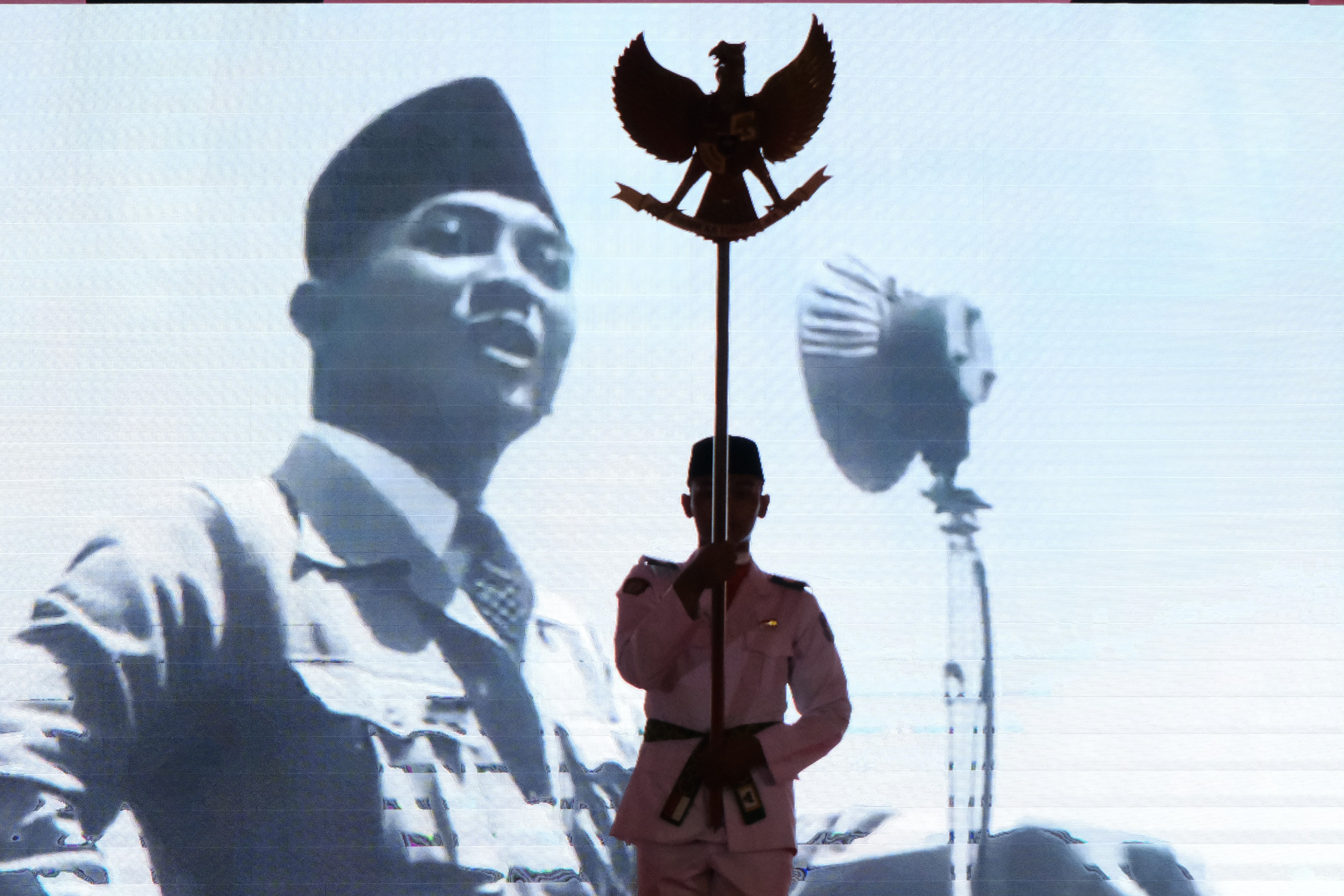 Seorang pemuda membawa Garuda Pancasila di depan layar yang menampilkan presiden pertama Indonesia Soekarno.