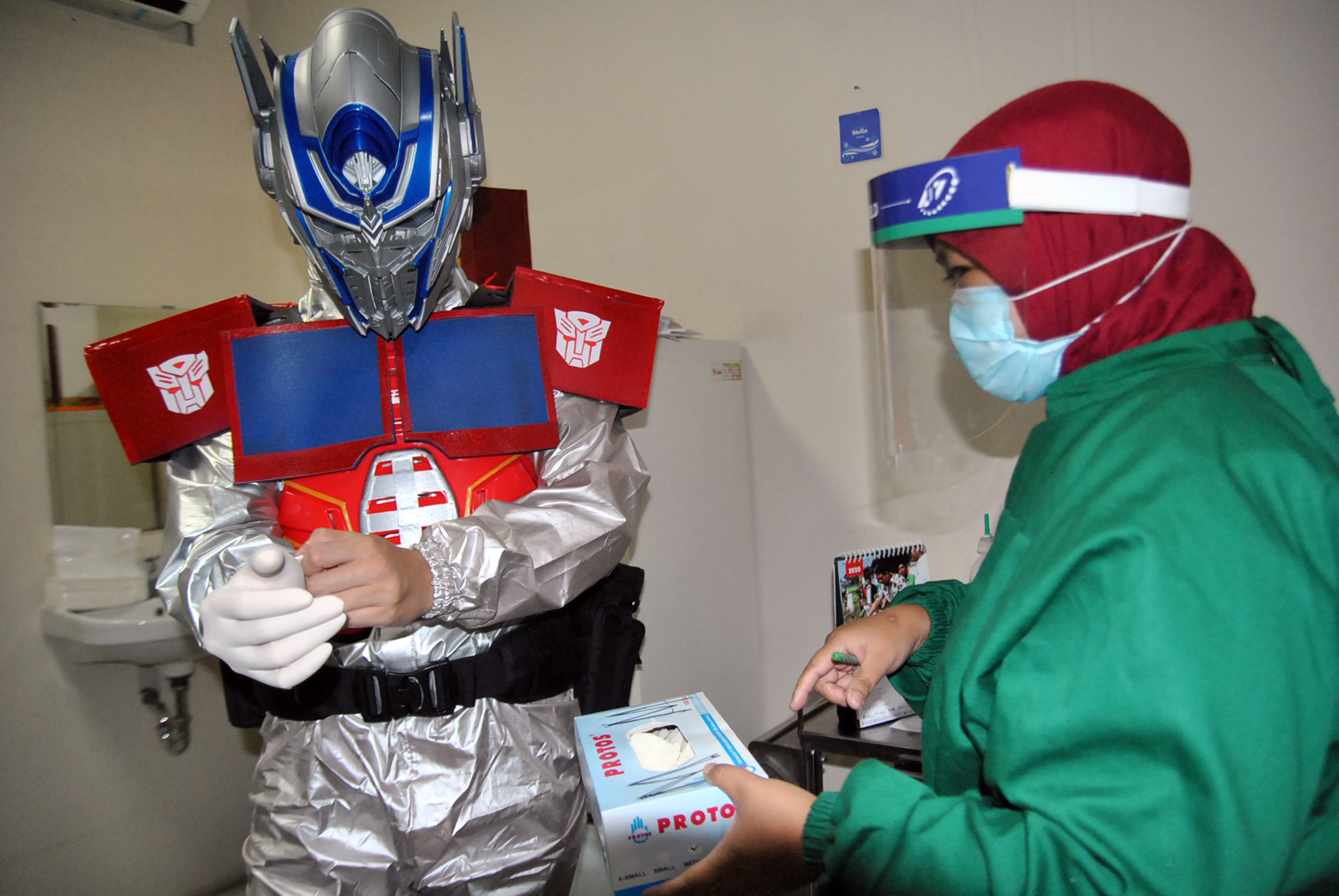 Seorang dokter spesialis (kiri) menggunakan alat pelindung diri (APD) kostum superhero Optimus Prime.