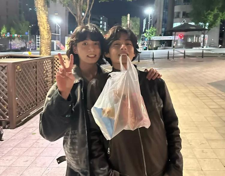 Potret V tersenyum mengigit sebuah plastik putih sambil dirangkul Jungkook dari instagram @thv