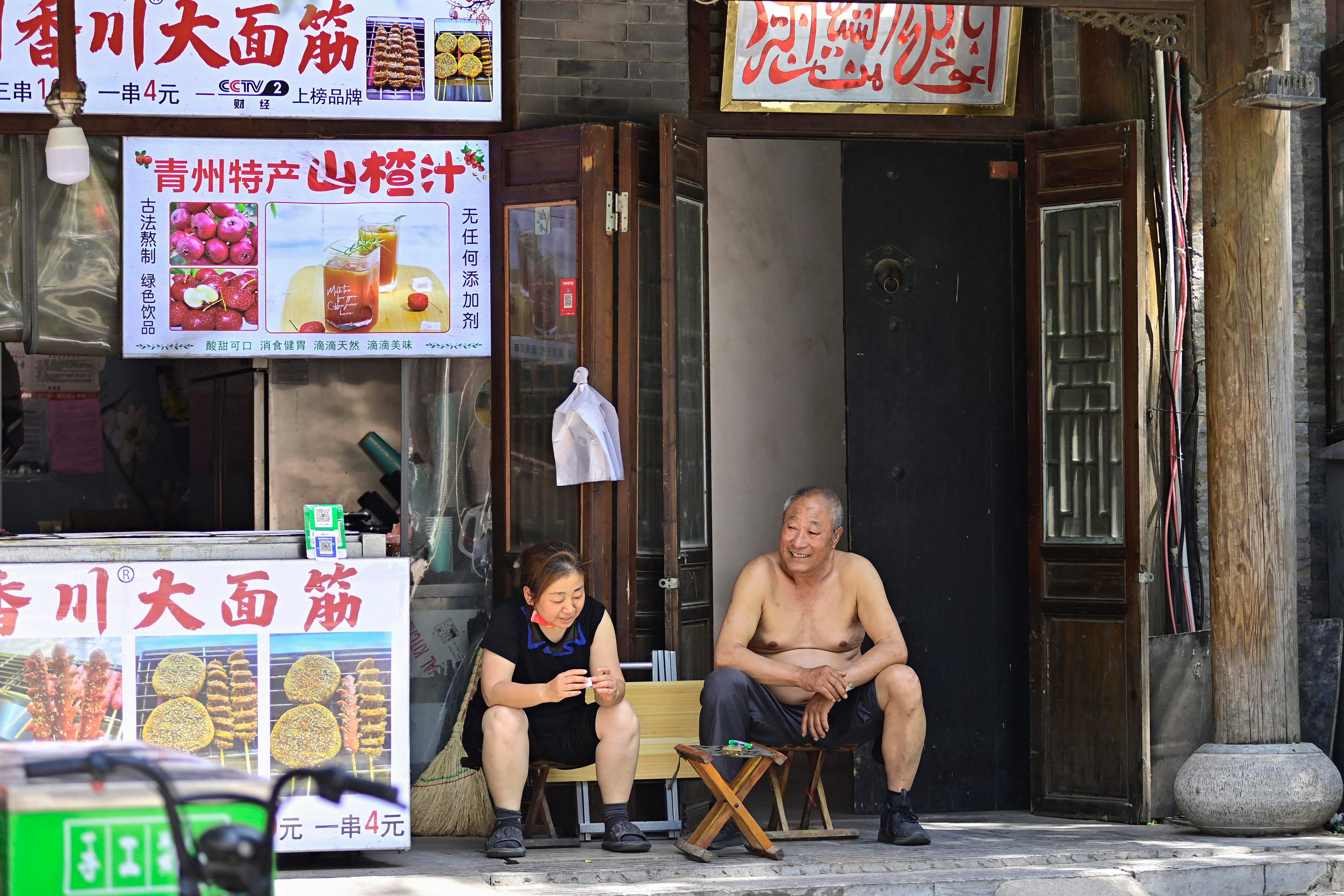 Warga berbincang di luar toko kawasan Qingzhou, Provinsi Shandong, di tengah meningkatnya suhu akibat gelombang panas.