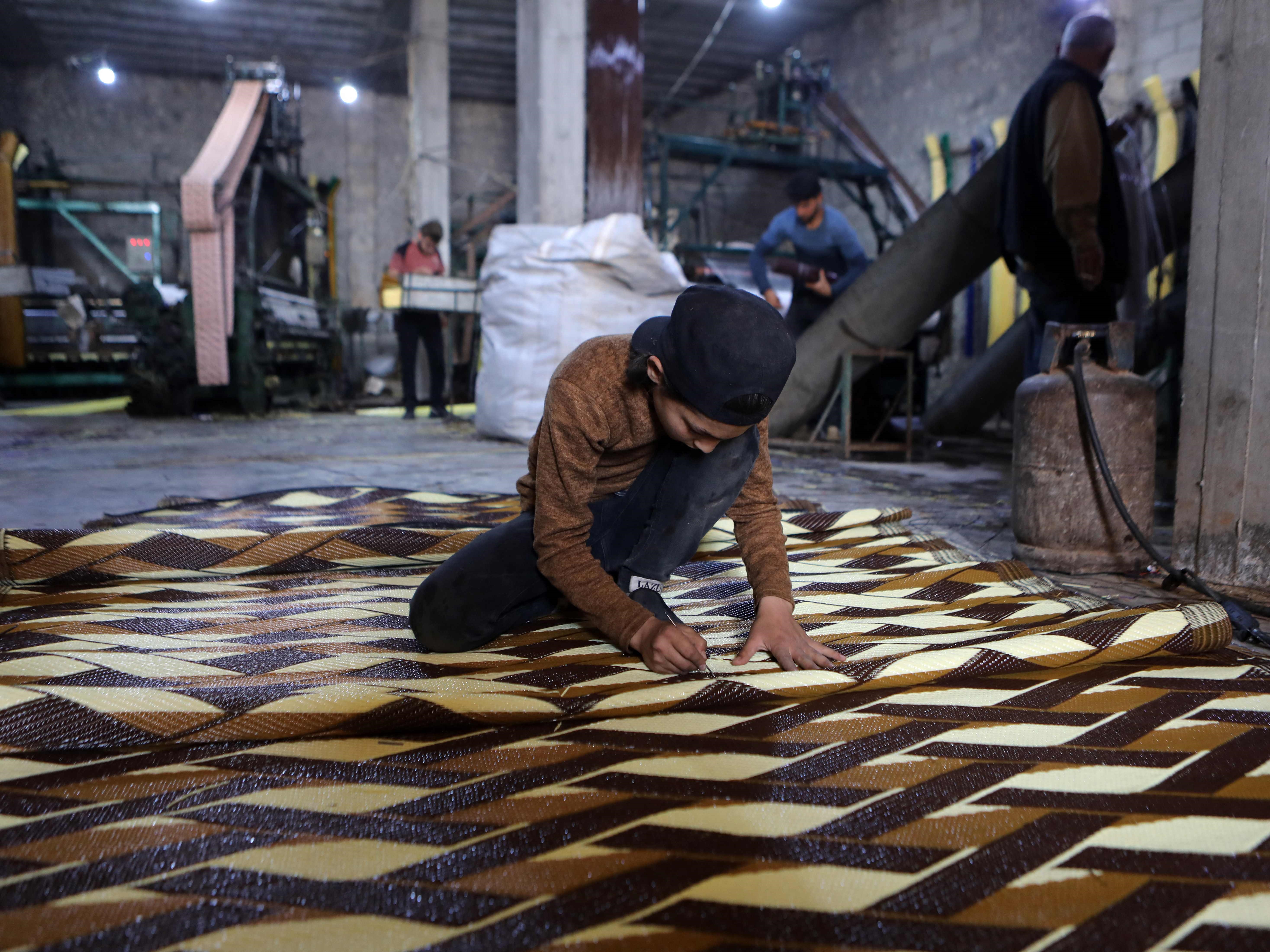 Seorang anak bekerja di pabrik pembuatan tikar dan permadani dari plastik daur ulang di Sarmada, Provinsi Idlib barat laut, Suriah.