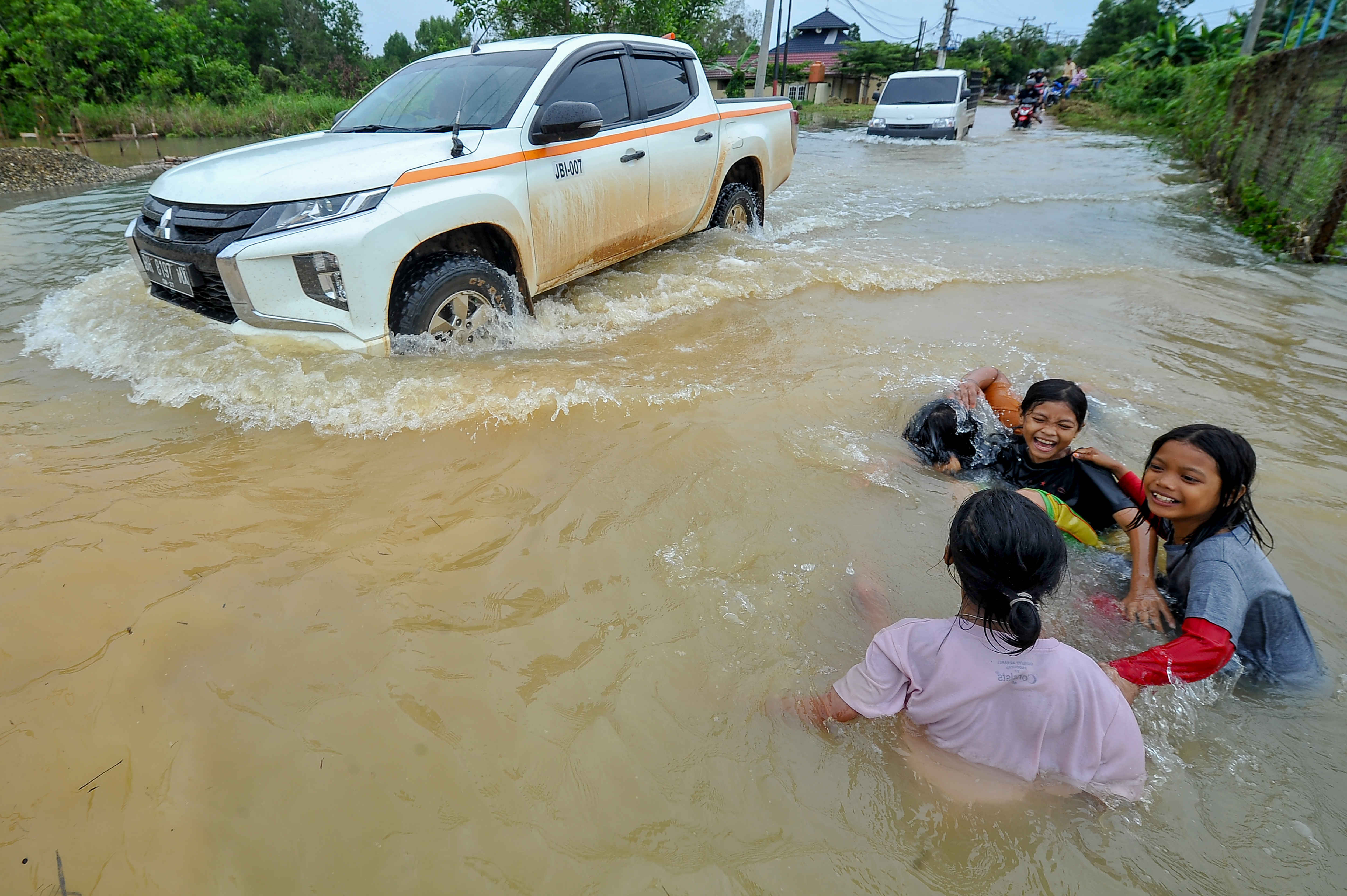 Ilustrasi: sejumlah bocah bermain air di dekat kendaraan yang menerobos jalan yang terendam banjir