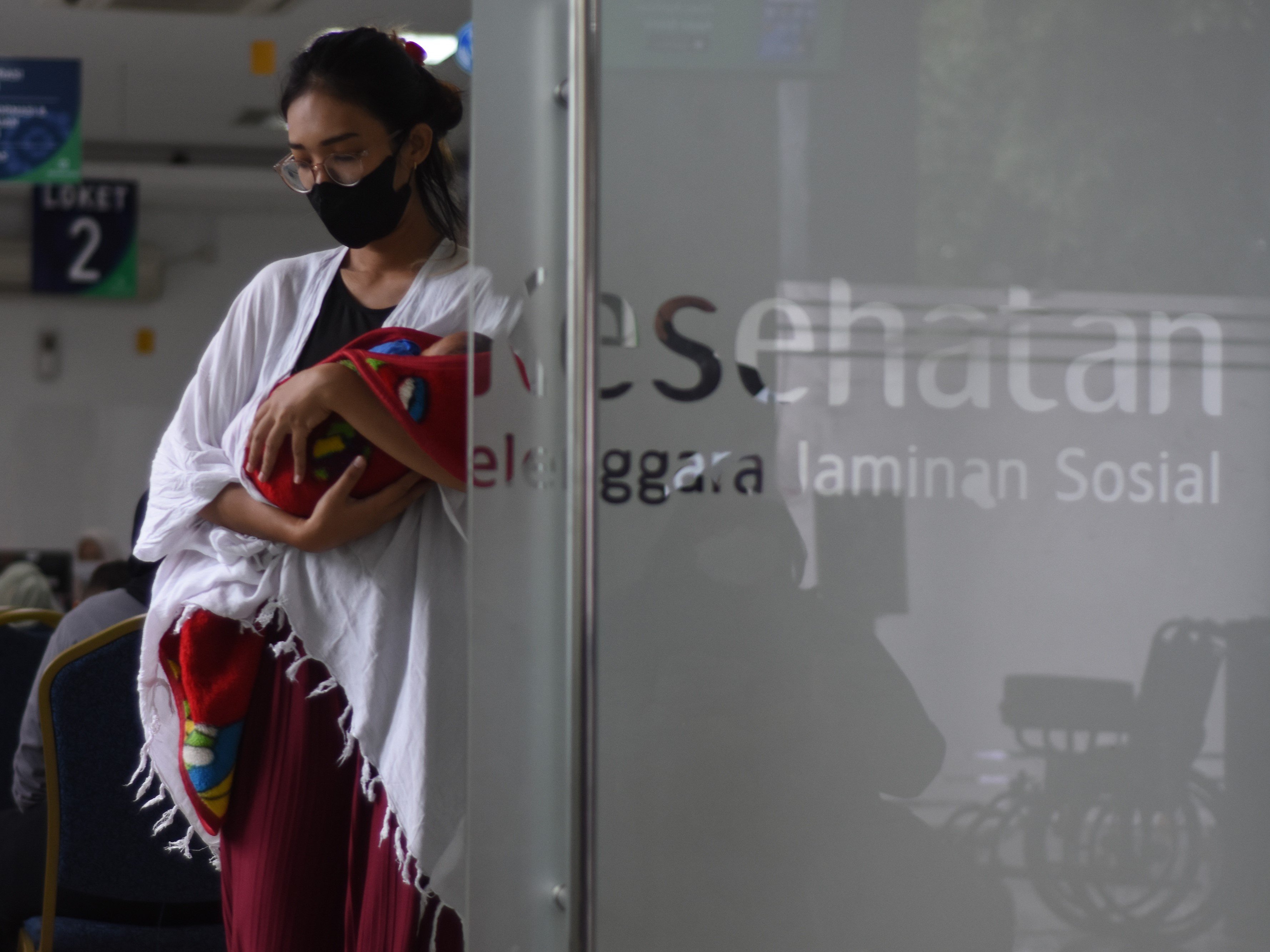Seorang ibu bersama bayinya antre mengurus layanan asuransi kesehatan di Kantor BPJS Kesehatan Cabang Jakarta Timur, Rawamangun, Jakarta.