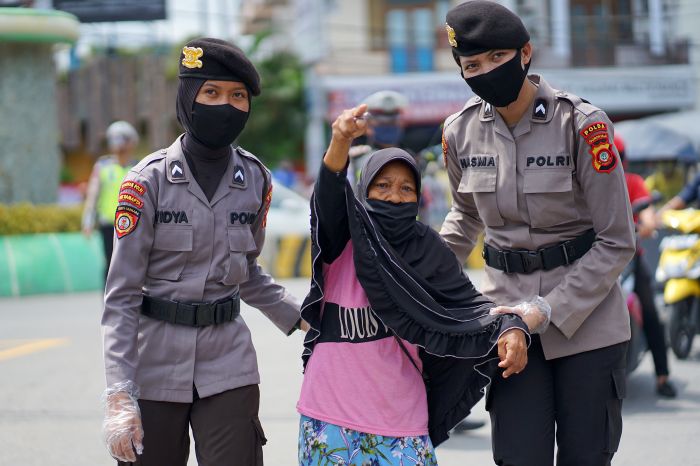 Dua polisi wanita (polwan) menuntun seorang nenek menyeberang jalan saat pembagian masker gratis di Kota Gorontalo.