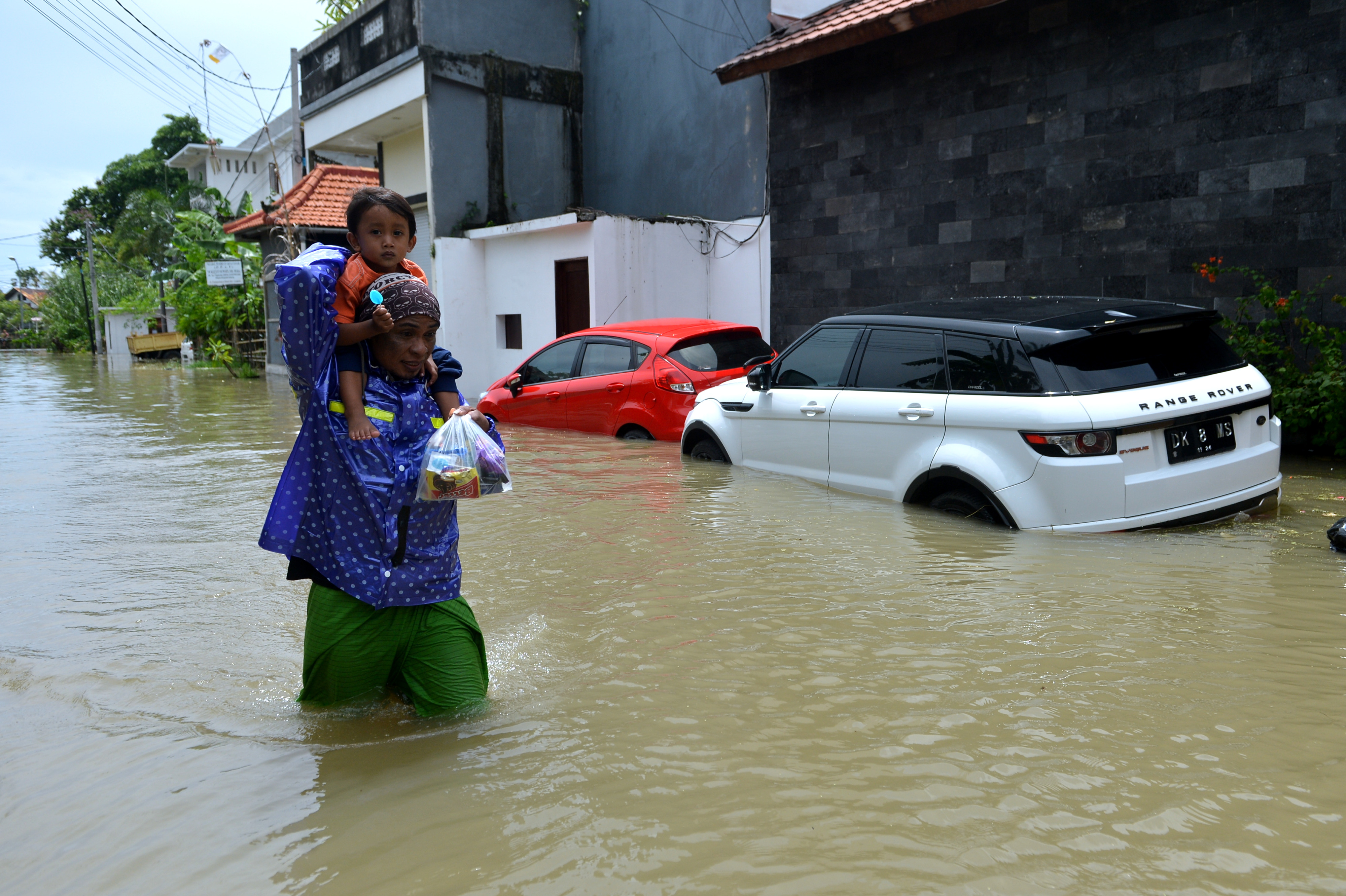 Warga berjalan menerobos banjir yang menggenangi kawasan Legian, Kuta, Badung, Bali, Senin (6/12/2021).