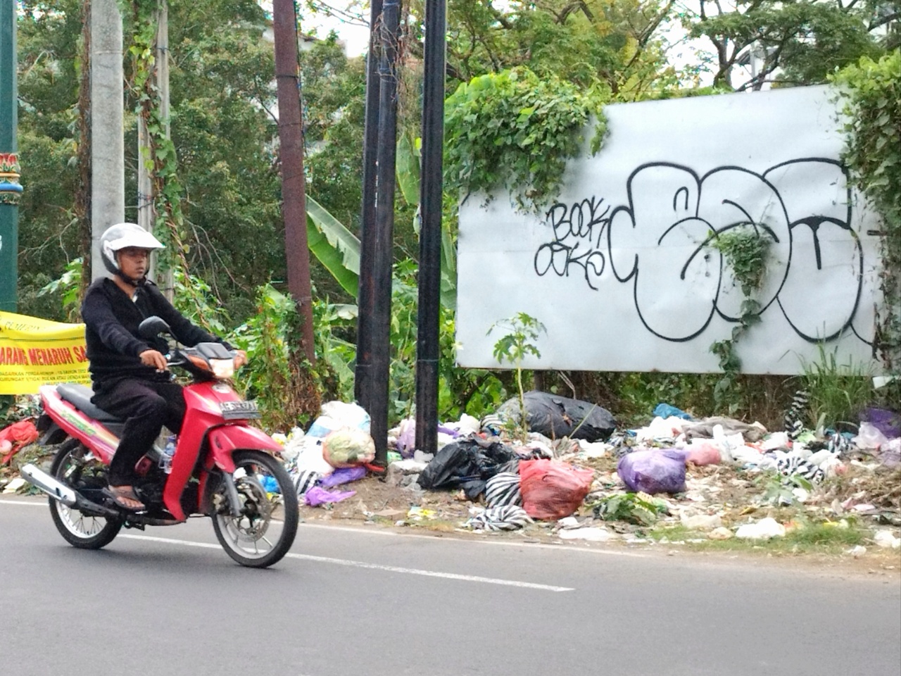 Warga melintas di dekat tumpukan sampah yang ada di TPS Gembira Loka