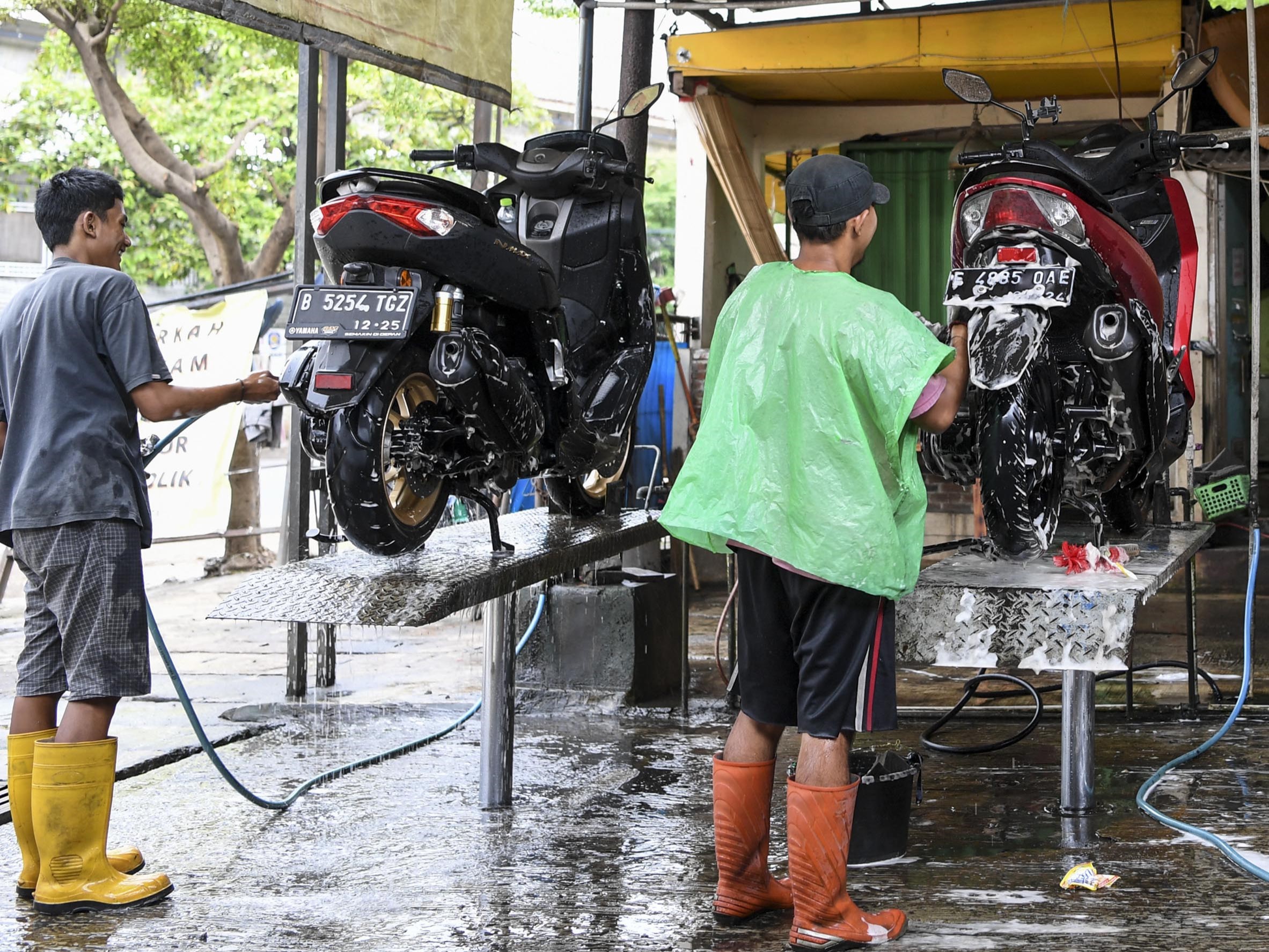 Pekerja mencuci motor milik pelanggan pada jasa cuci motor di kawasan Manggarai, Jakarta, Selasa (3/1/2023).