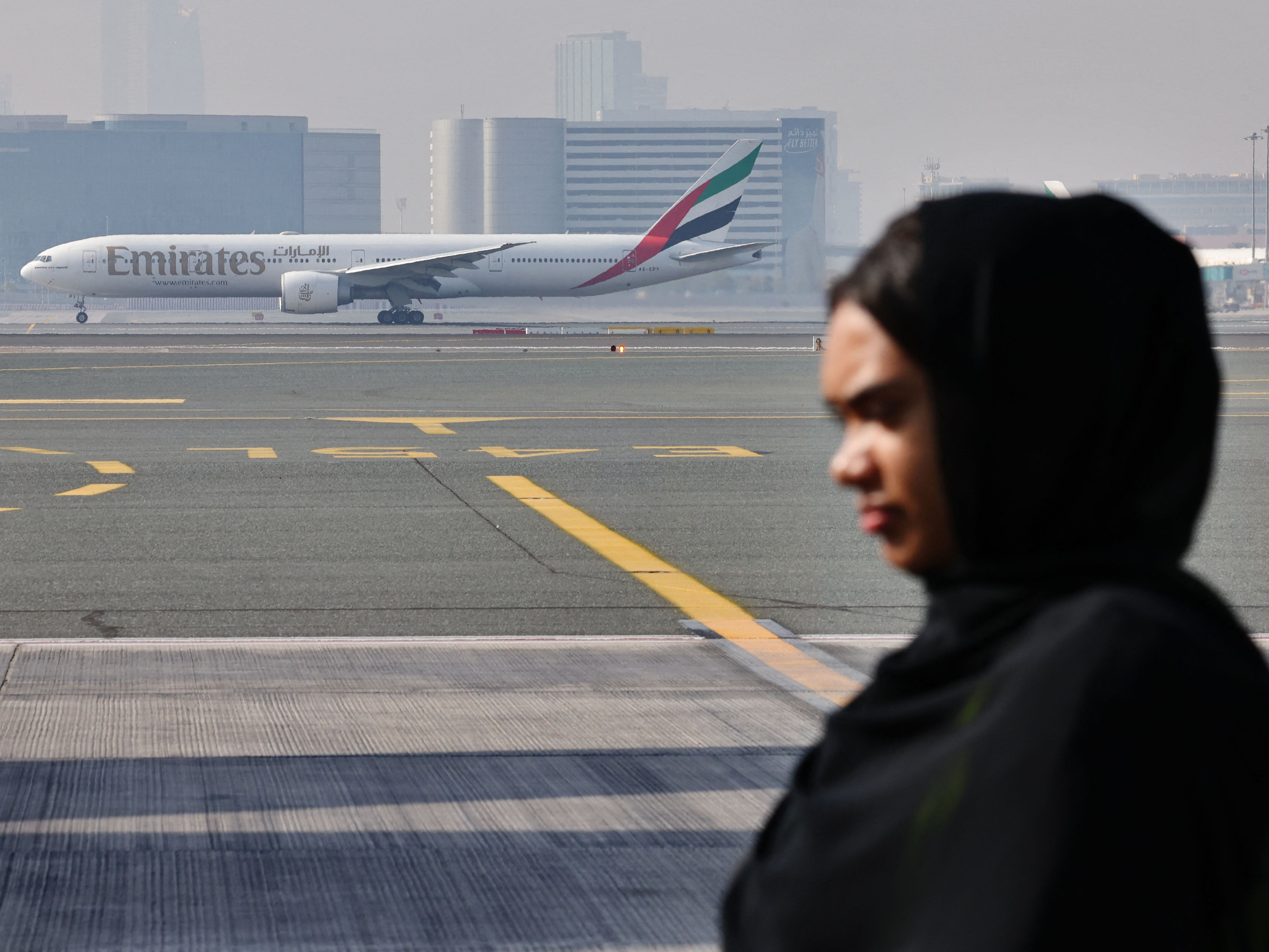 Seorang wanita Emirat berlatar pesawat Emirates Boing 777-300ER di landasan Bandara Internasional Dubai.