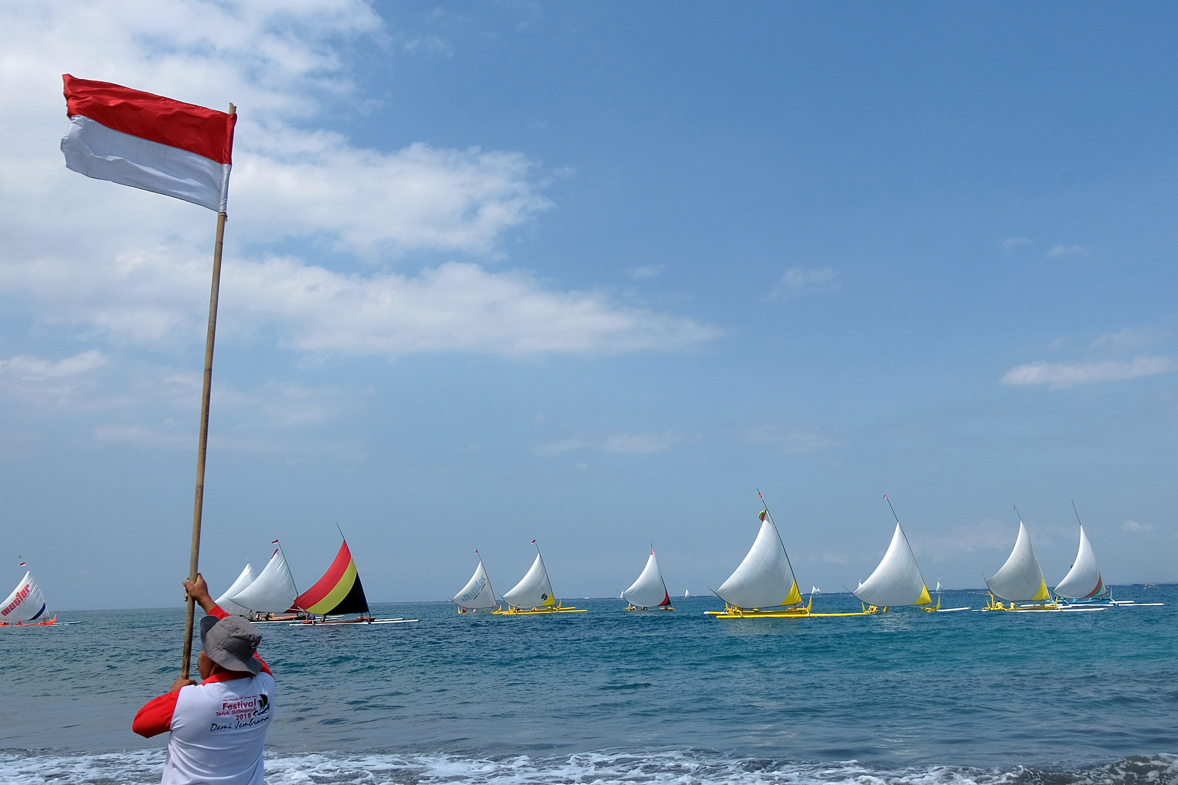 Panitia mengibarkan bendera merah putih saat berlangsungnya lomba perahu layar Selat Bali di Pantai Gilimanuk, Jembrana, Bali.