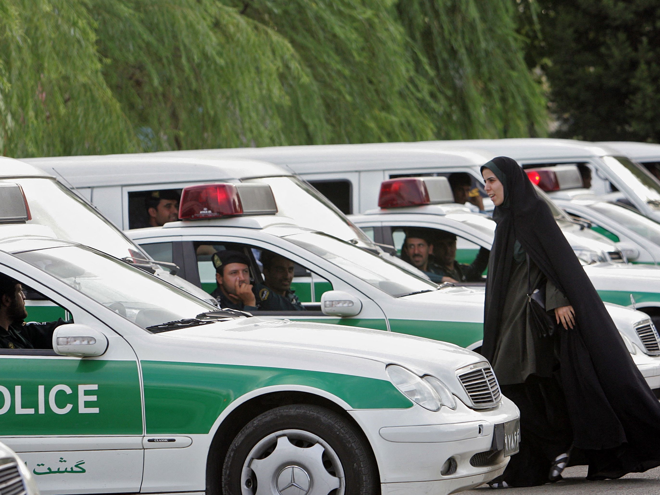 Seorang polisi wanita Iran (kanan) berjalan di antara kendaraan polisi moral.